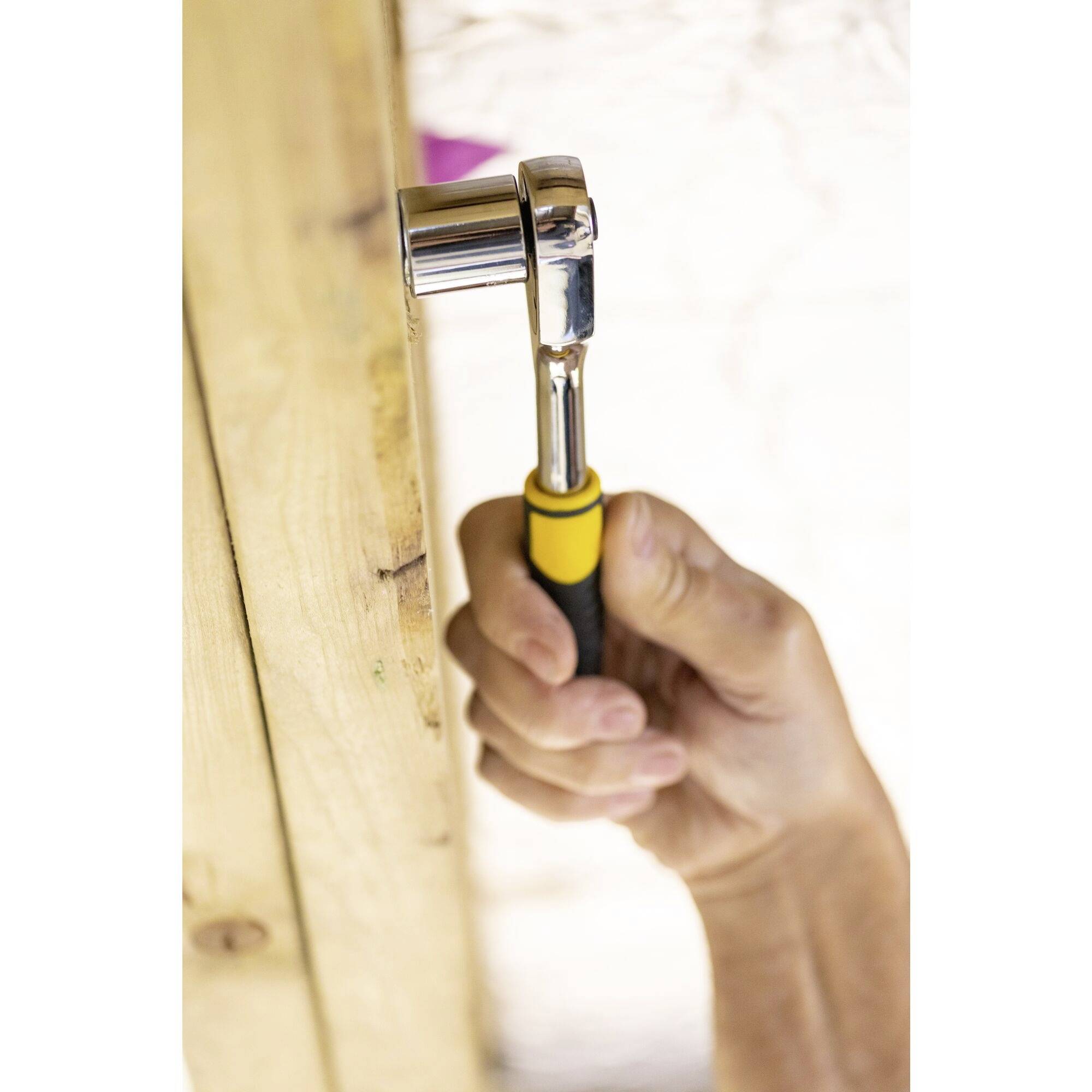 A hand is using a ratchet spanner to turn a screw into a wooden board.
