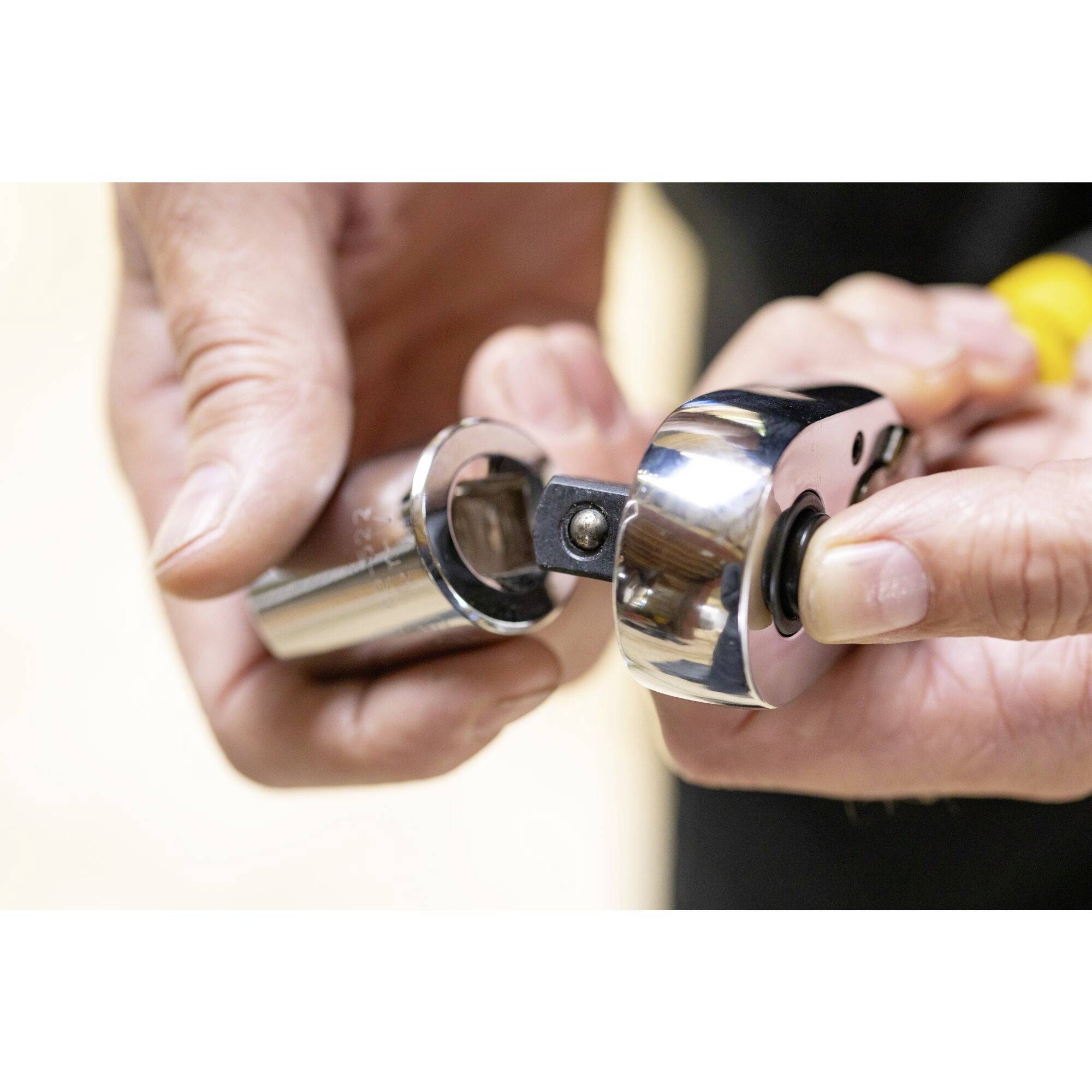 Two hands are operating a silver cap lifter to remove a sealed capsule.