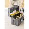 An open toolbox on a wooden floor, filled with yellow compartments, screwdrivers, and pliers. A hand reaches inside.