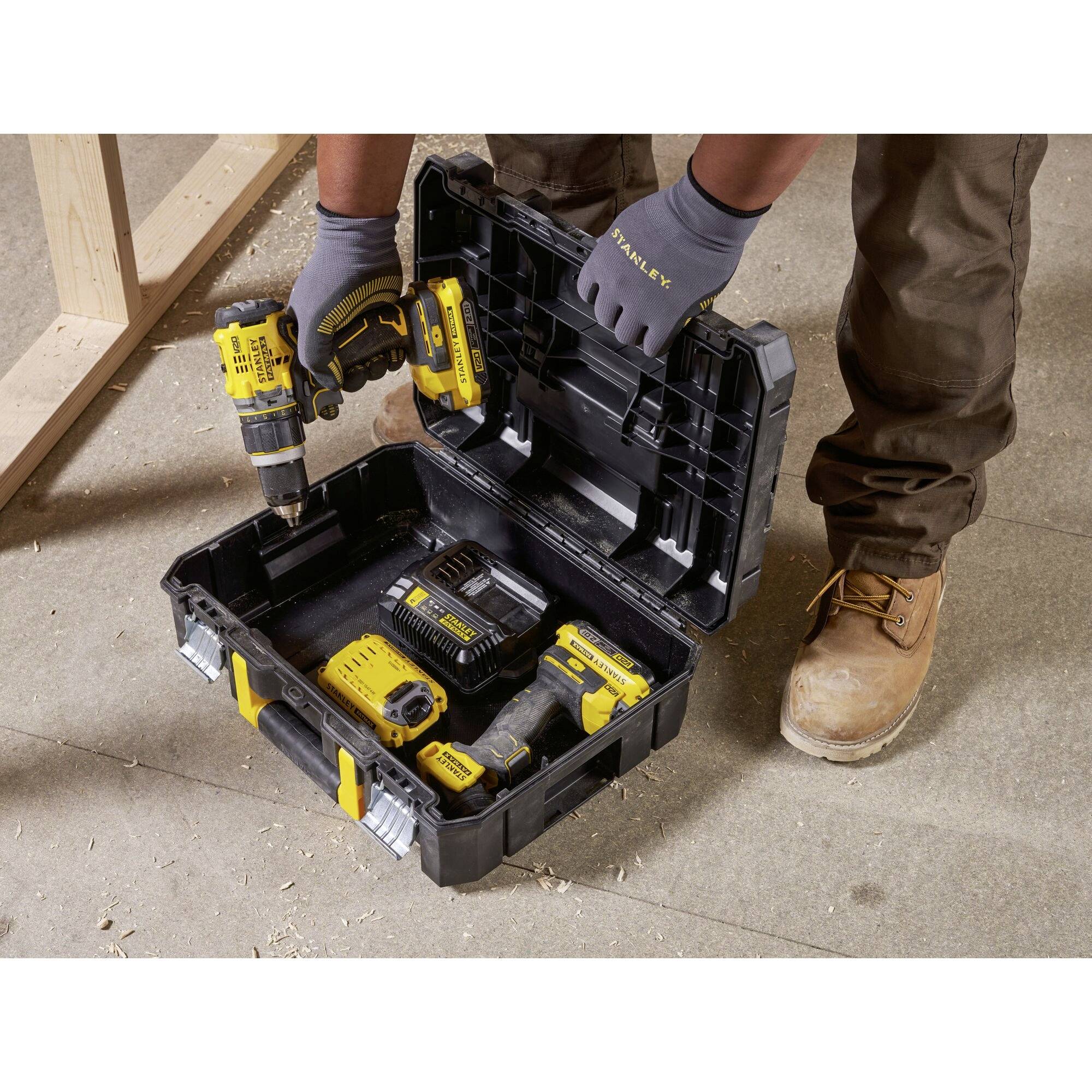 A person in work attire is unpacking a drill from a tool case. Wooden beams are visible in the background.