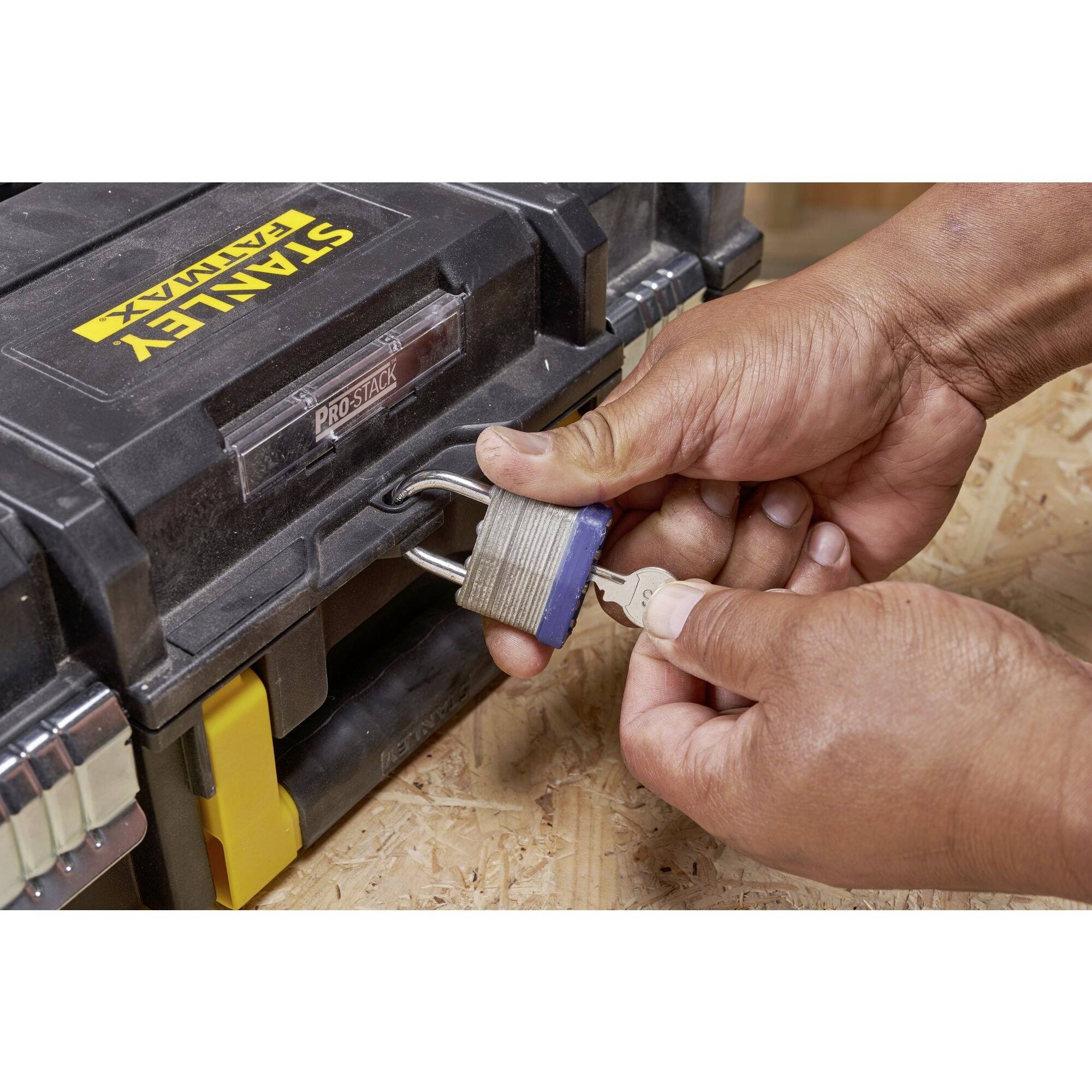 A person unlocks a padlock with a key. The lock is securing a toolbox on a workbench.