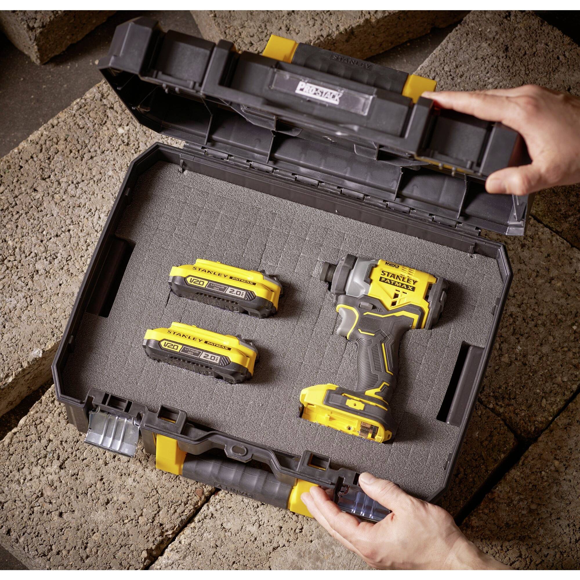 A tool case with a hand drill and two rechargeable batteries. A hand is opening the case.