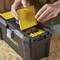 A person opens the lid of a black toolbox with a yellow drawer to remove screws and wall plugs from a wooden surface.