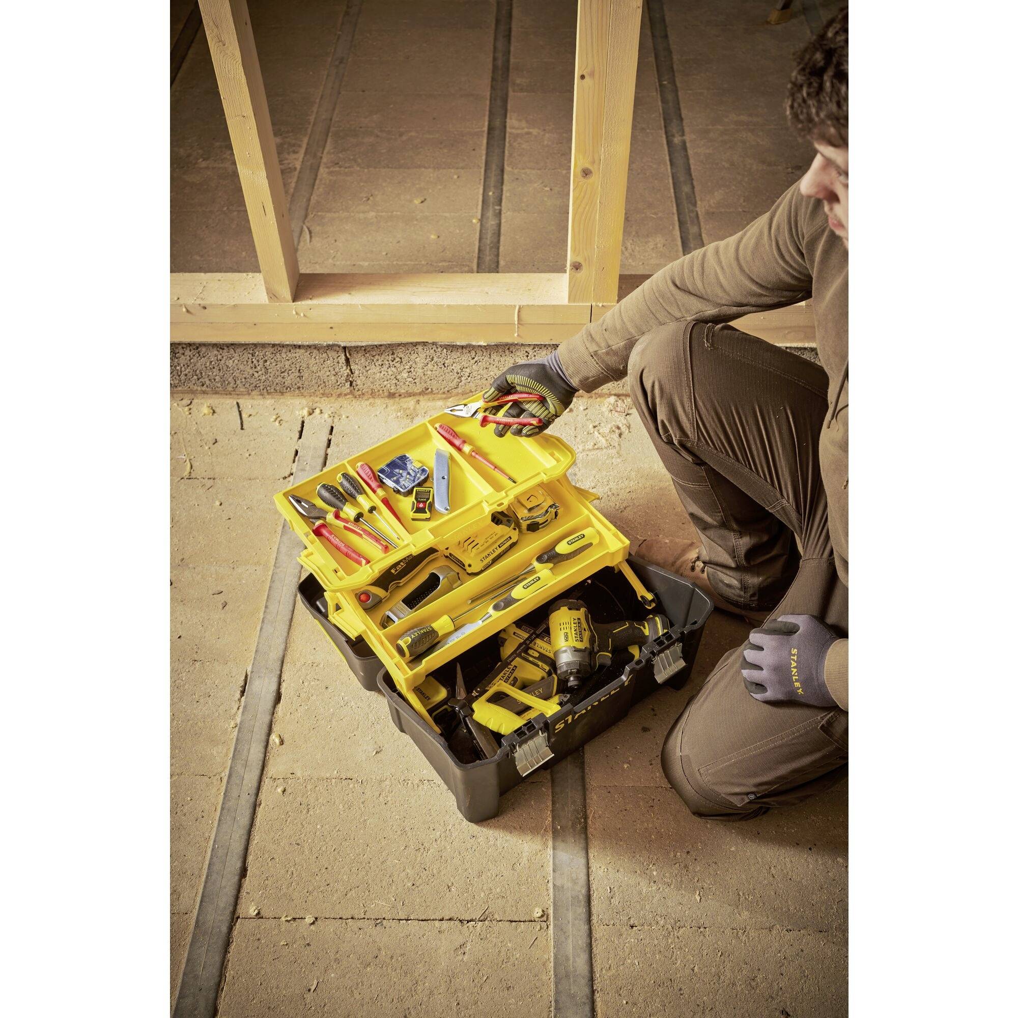 A tradesman is kneeling in front of an open toolbox displaying various tools. He is holding a multimeter in his hand.