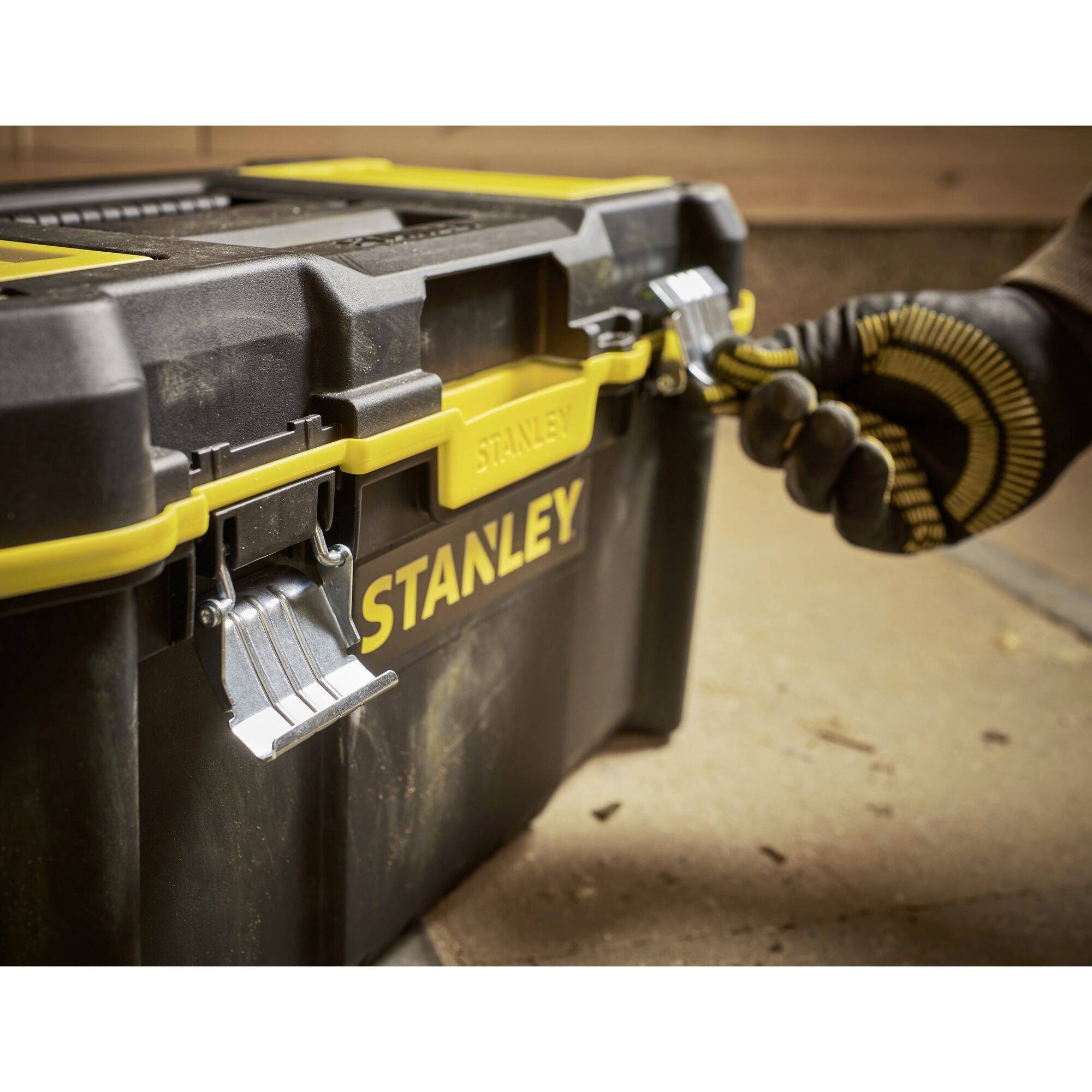 A person opens a black toolbox with yellow details, labelled 'Stanley', while wearing gloves.