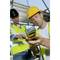 Two construction workers in hi-vis vests and hard hats are working on a building project. One is holding a tool in his hand, while the other is pointing.