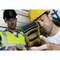 Two construction workers in hard hats and high-visibility vests are using a laser distance measuring device on a building site to carry out precise measurements.