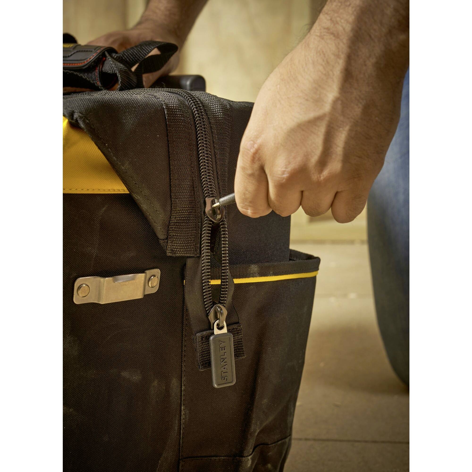 A hand pulls the zip of a black bag with yellow accents. The zip has a keyring attached.