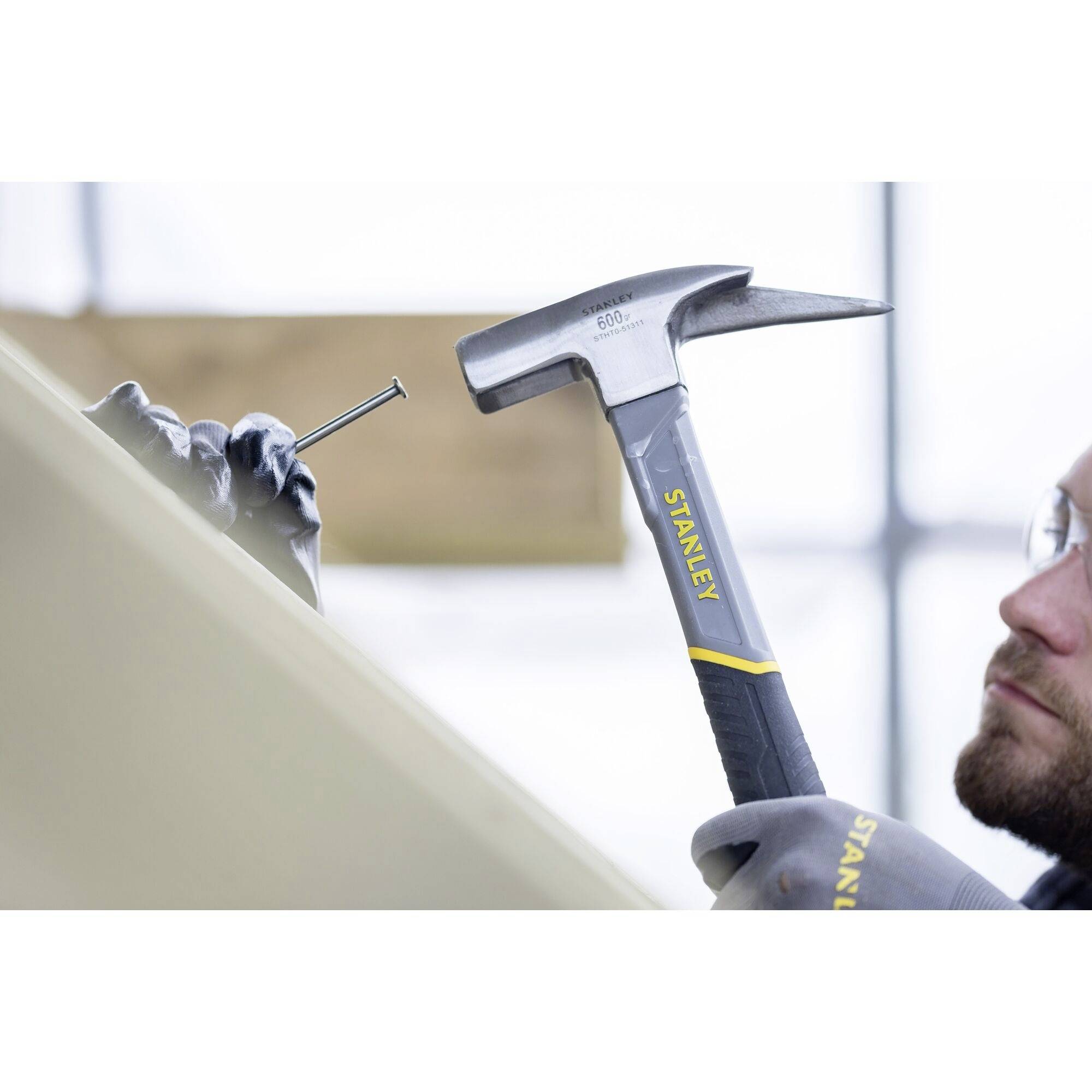 A person is hammering a nail into wood. The hammer is labelled 'Stanley'.