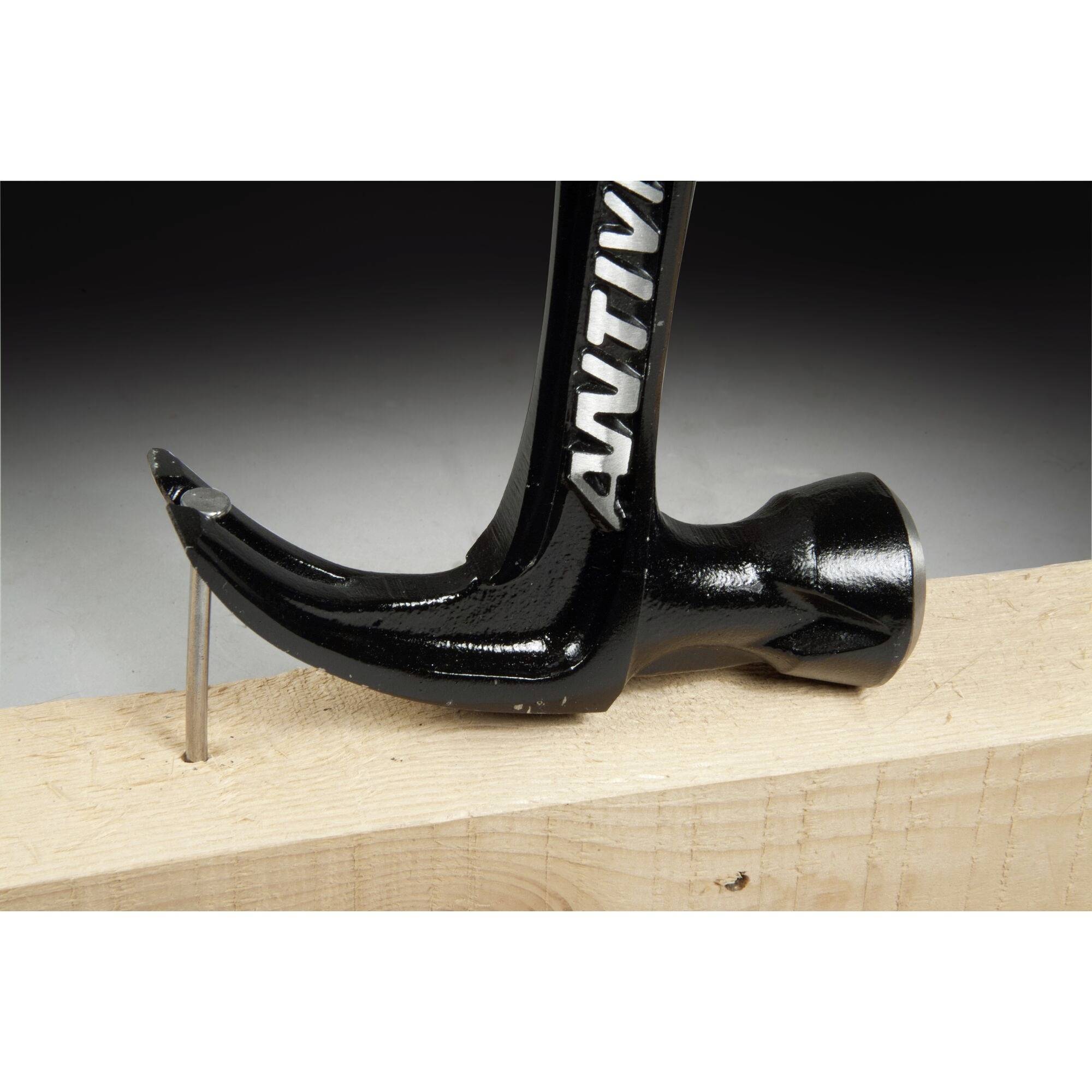 A hammer head pulls a bent nail out of a wooden board.