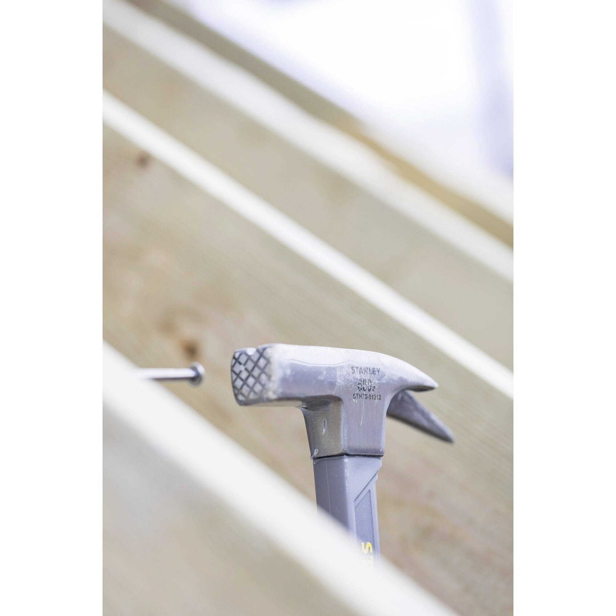 Hammer and nail on a wooden beam, ready for use. The hammer head is pointing to the left, the nail slightly angled.