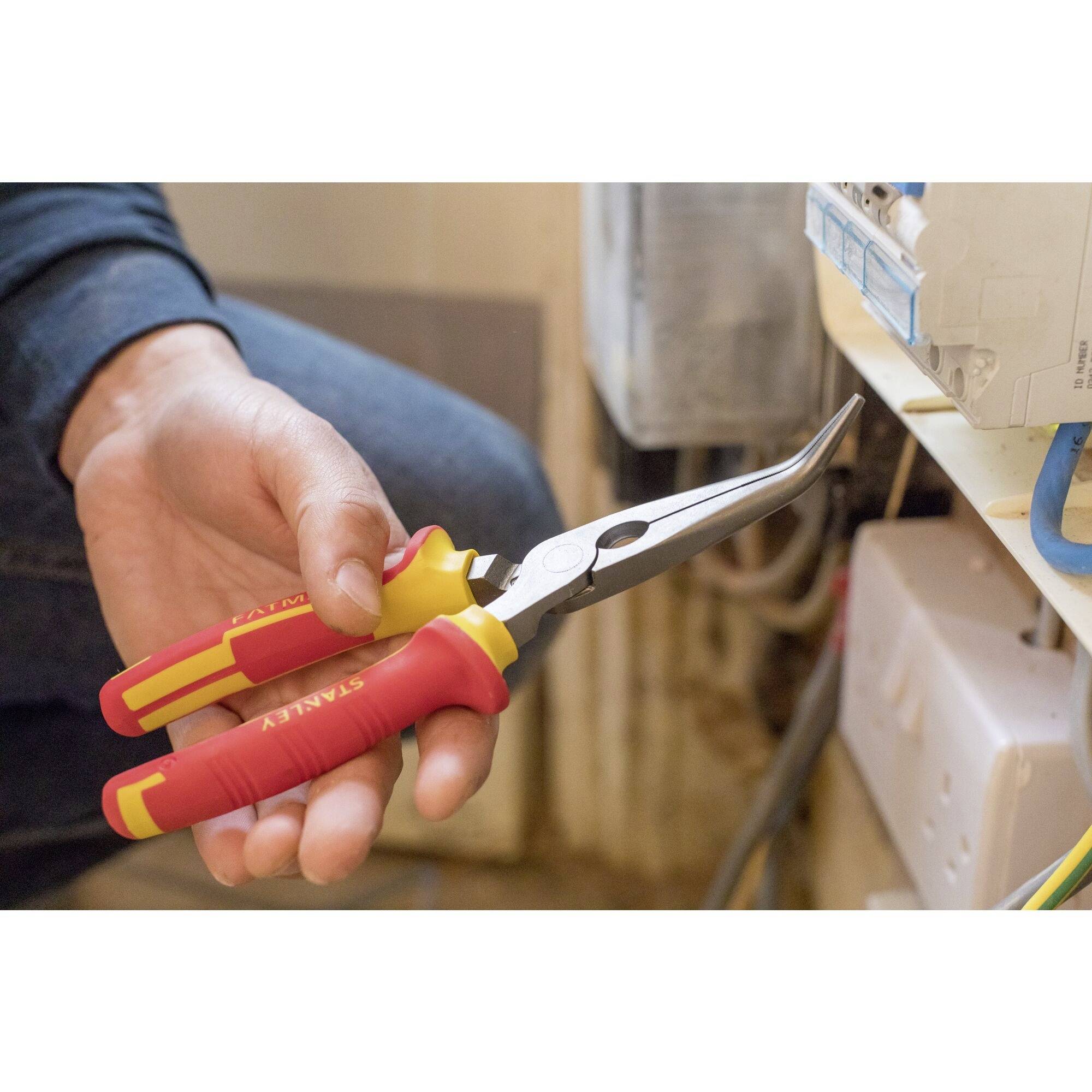 A person is holding a red pair of pliers and working on an electrical junction box. The pliers have red handles with yellow accents.
