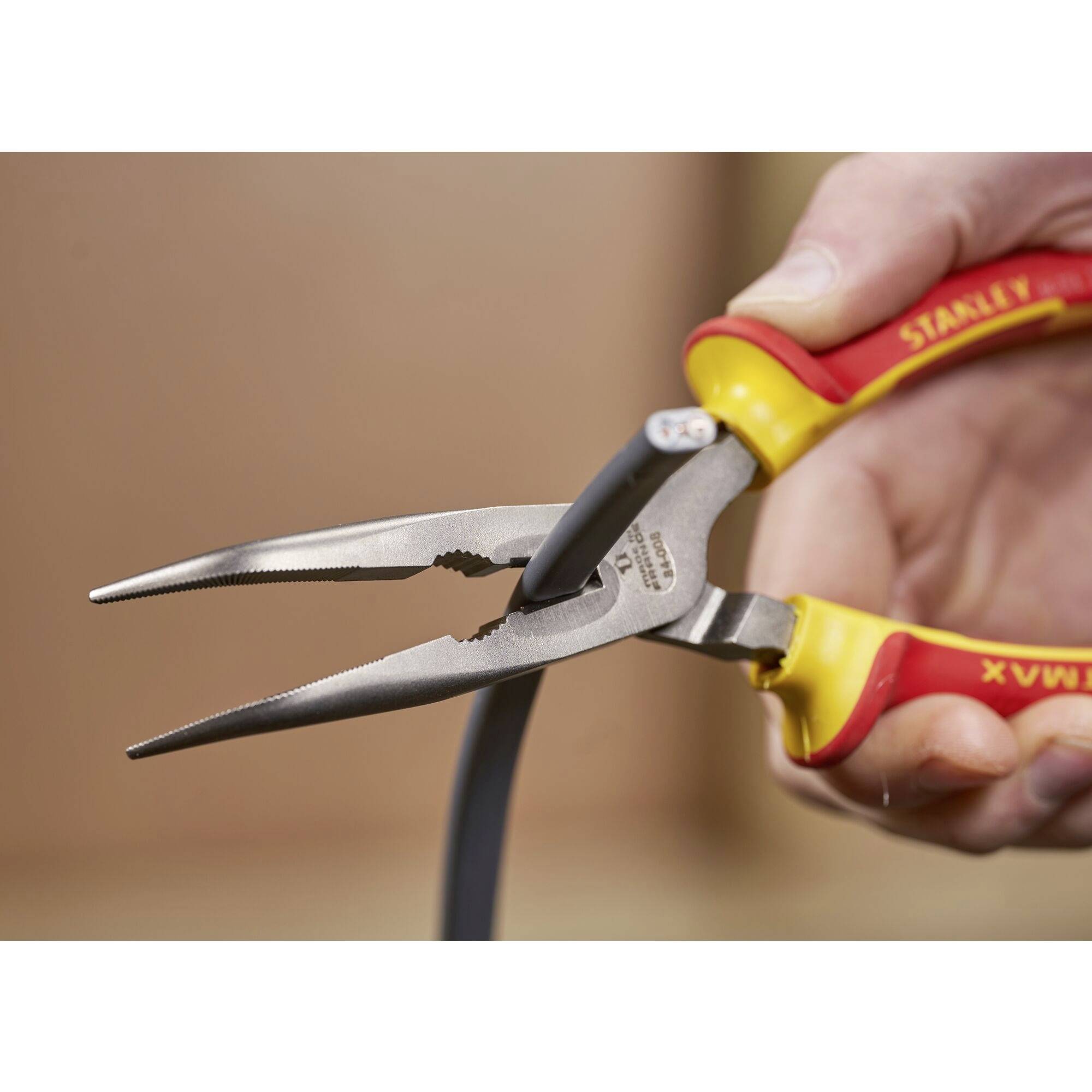 A hand is holding a combination pliers with red and yellow handles, cutting a black cable.