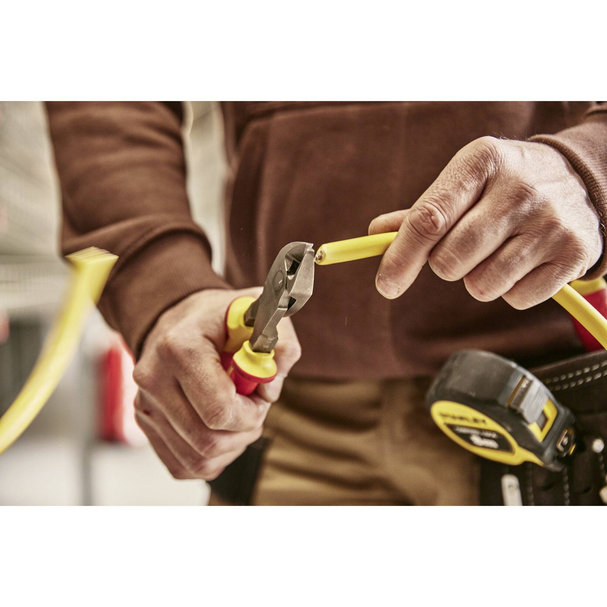 A tradesman cuts a yellow cable with pliers. A tape measure on his belt is blurred in the background.