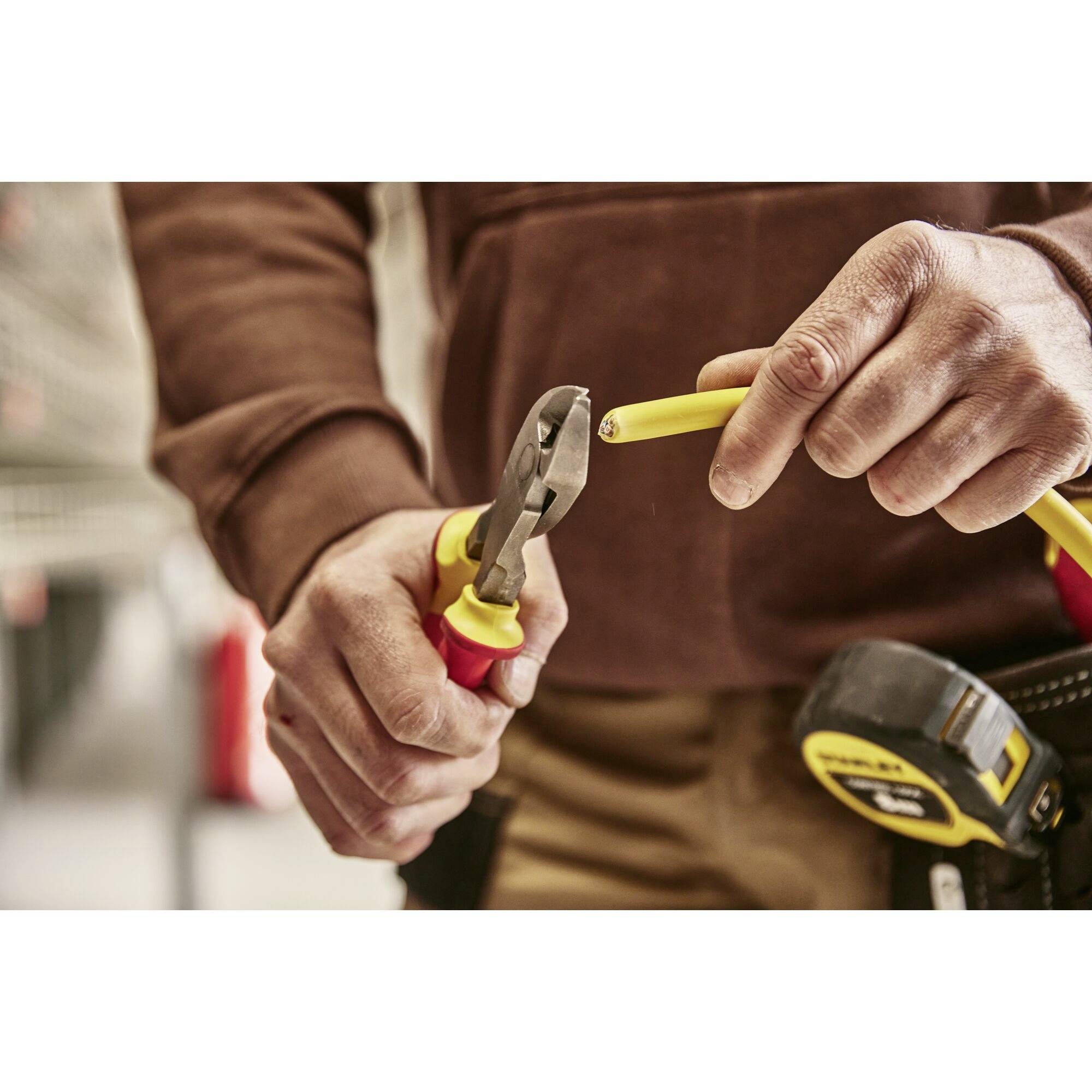 A person is cutting through a yellow cable with a red pair of pliers.