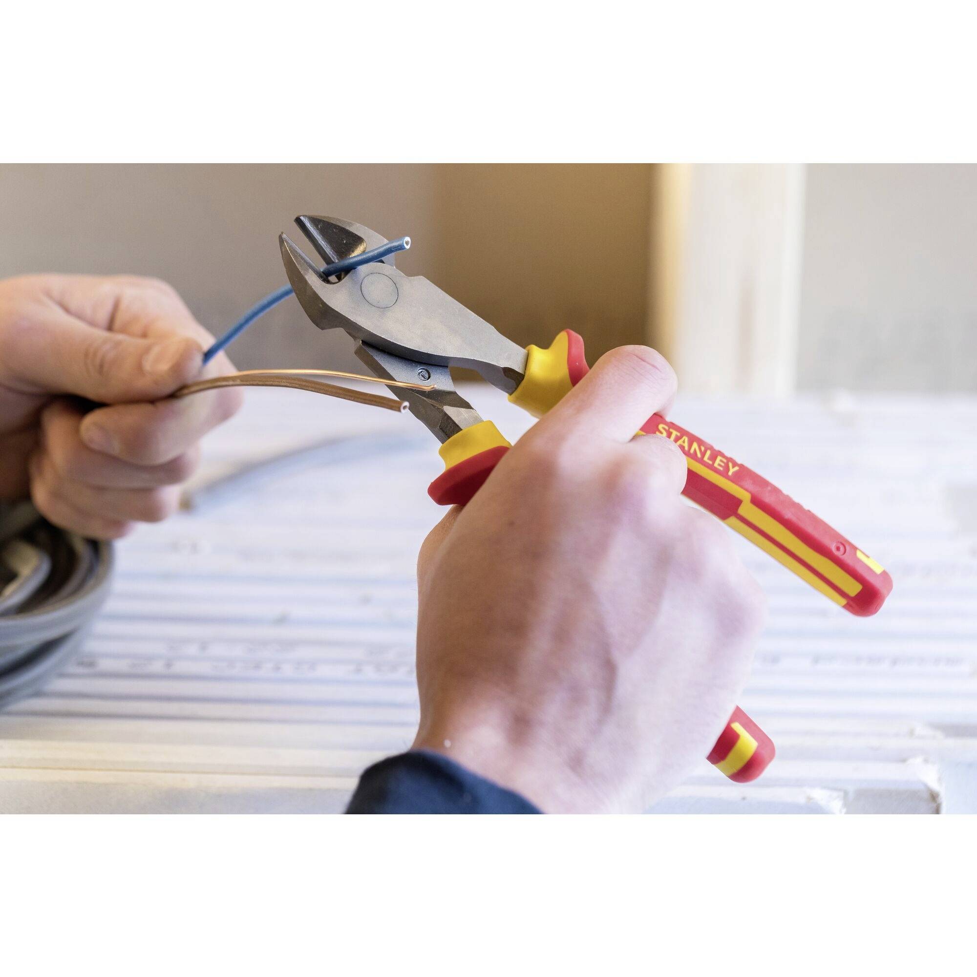 Hands are holding a cable cutter and cutting a cable. Additional cables can be seen in the background.