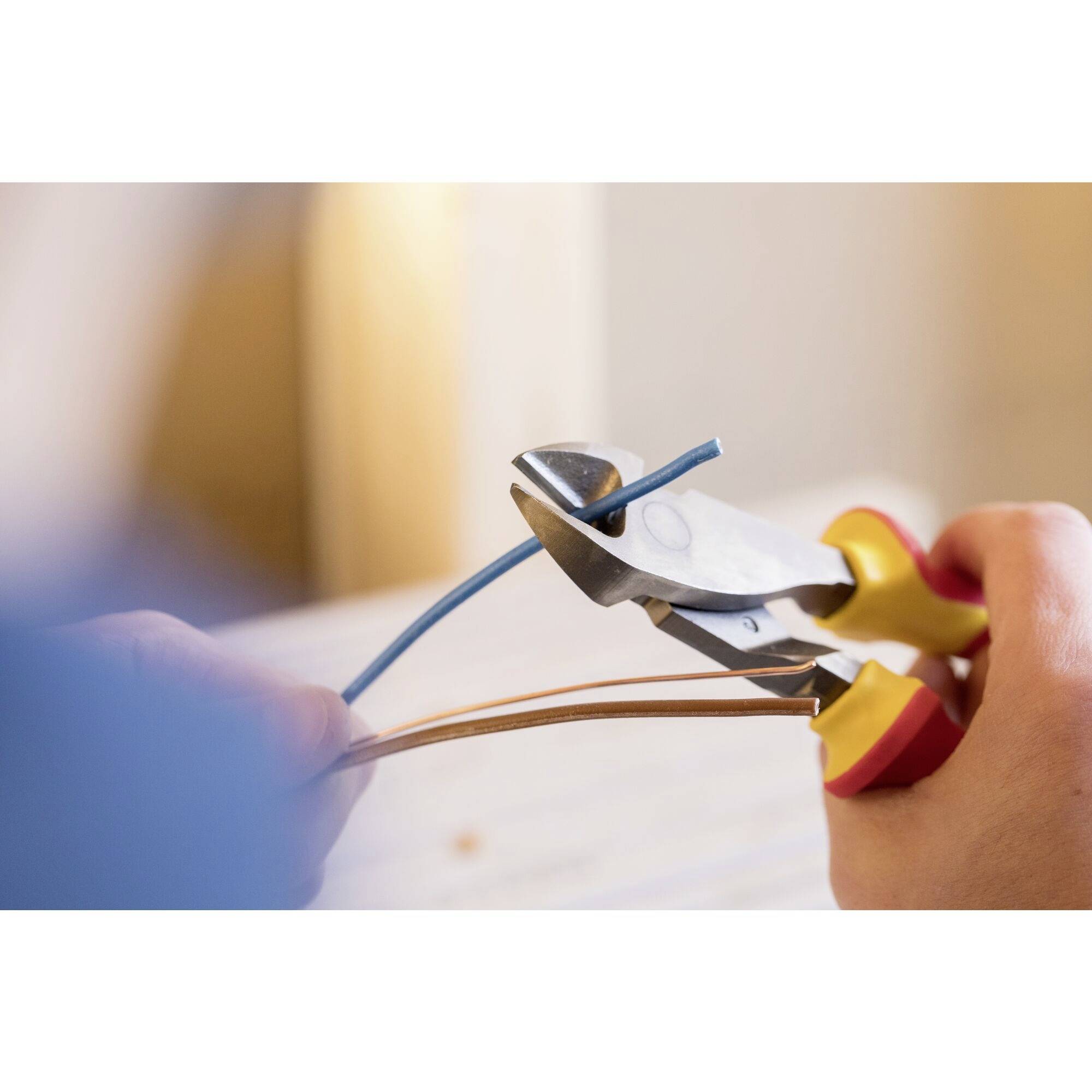A person is cutting a blue cable with wire cutters. In the background, a blurred room can be seen.