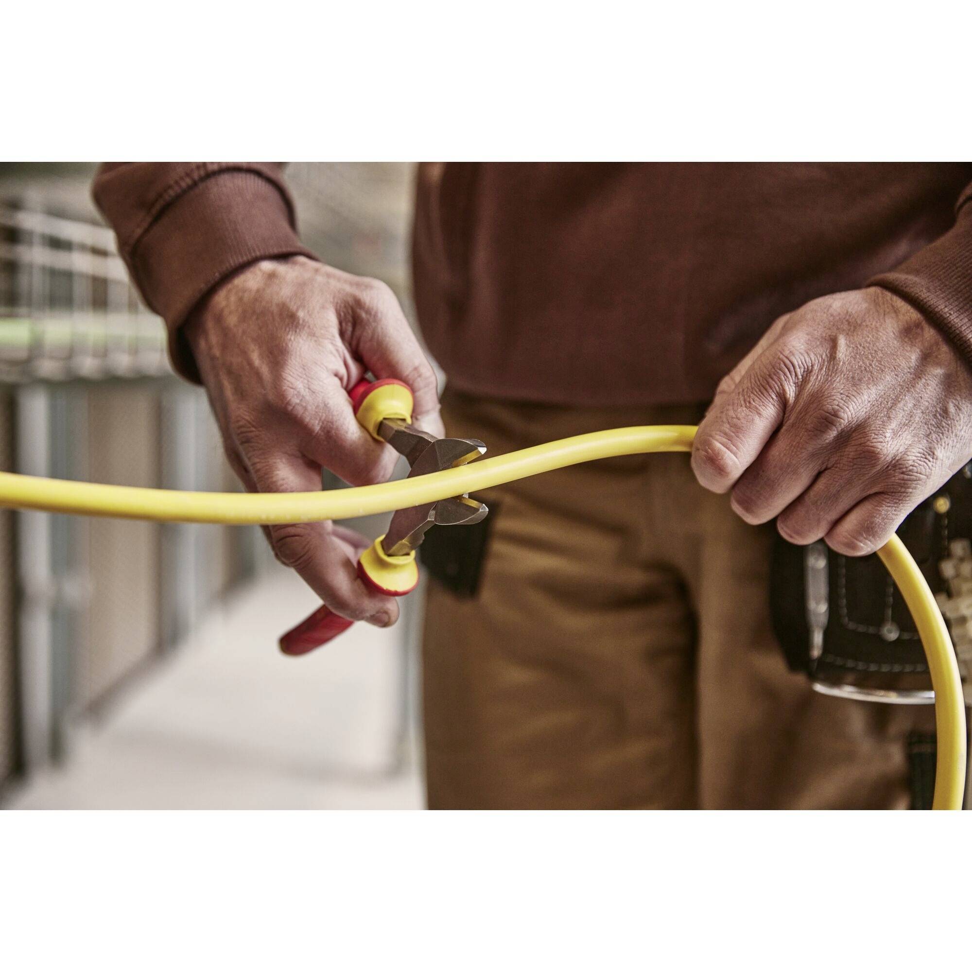 A person is using side cutters to slice through a thick, yellow cable. The scene suggests electrical work.