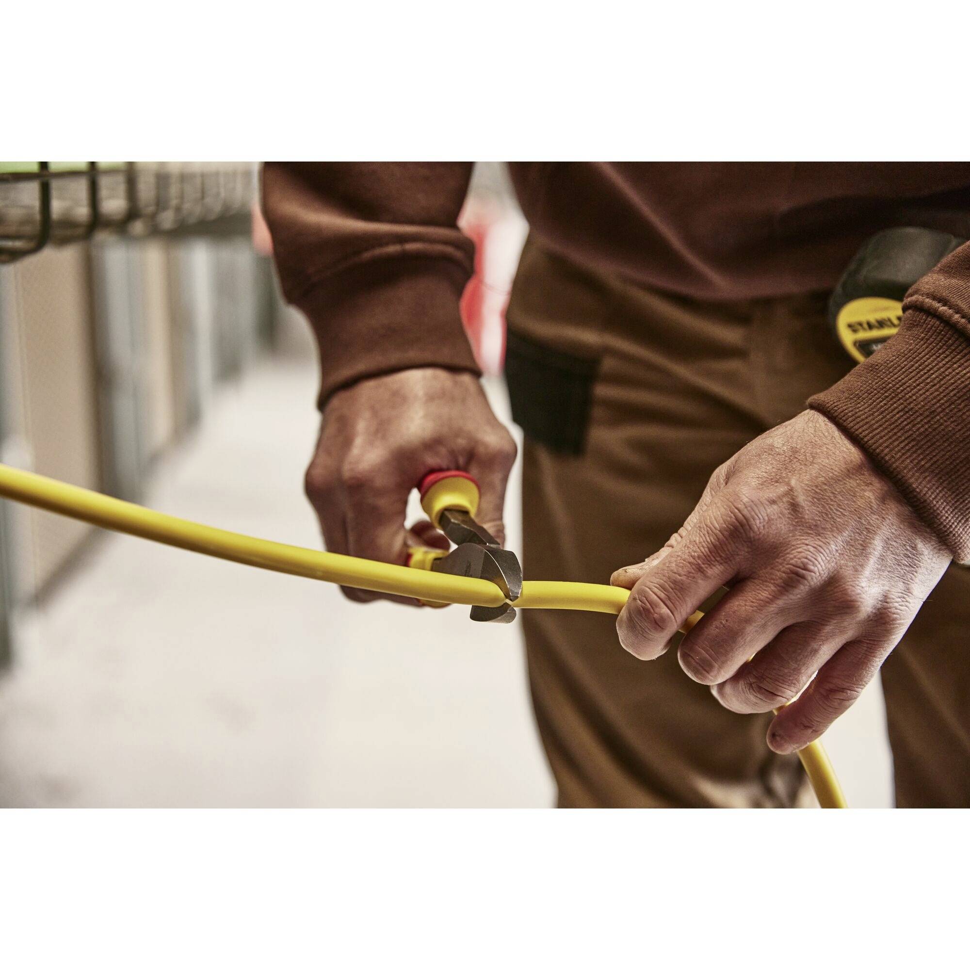 'Person cutting yellow cable with side cutters, focus on hands. Blurred background in the room.'