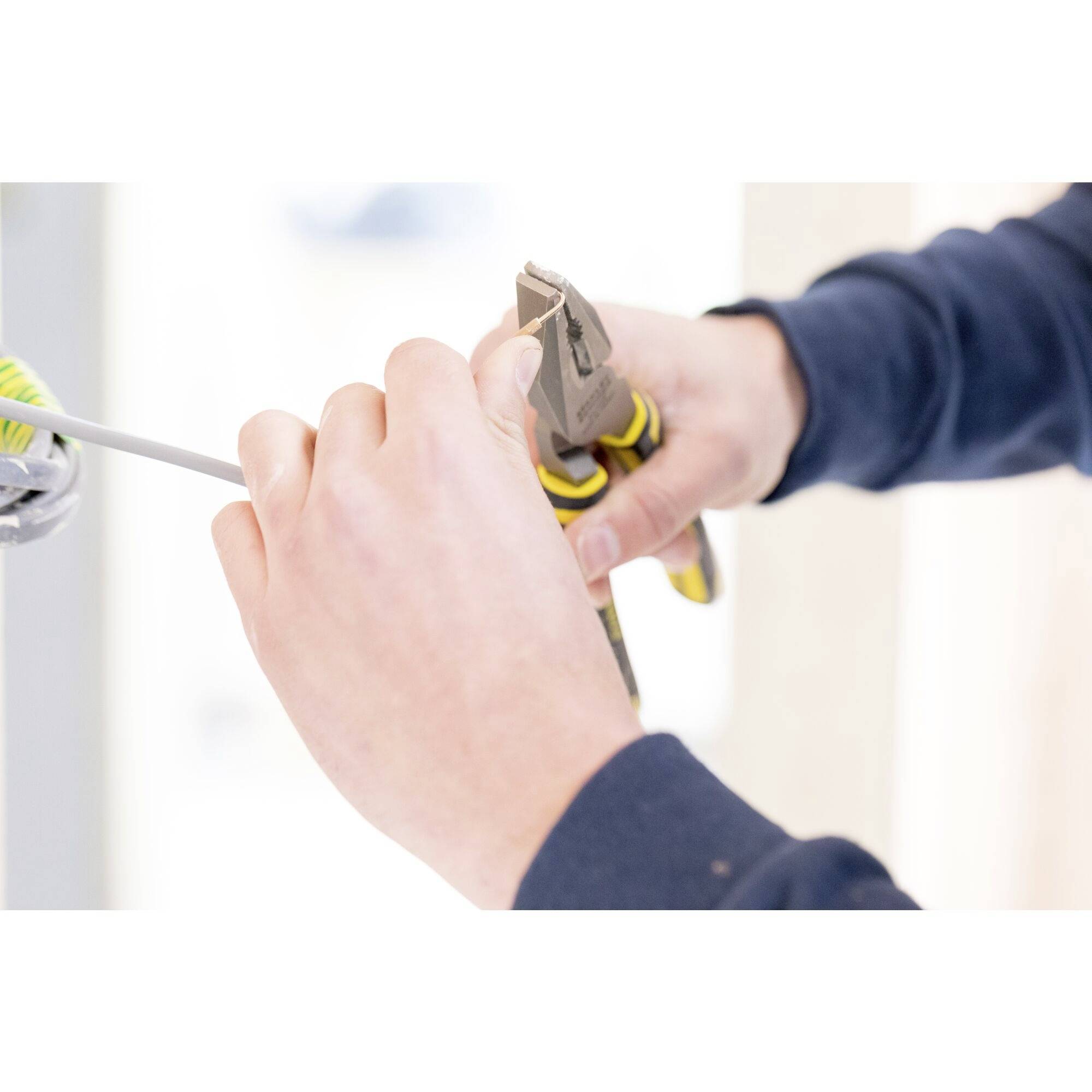 A person is using wire cutters to cut a cable. Close-up of hands, tool and cable in focus.