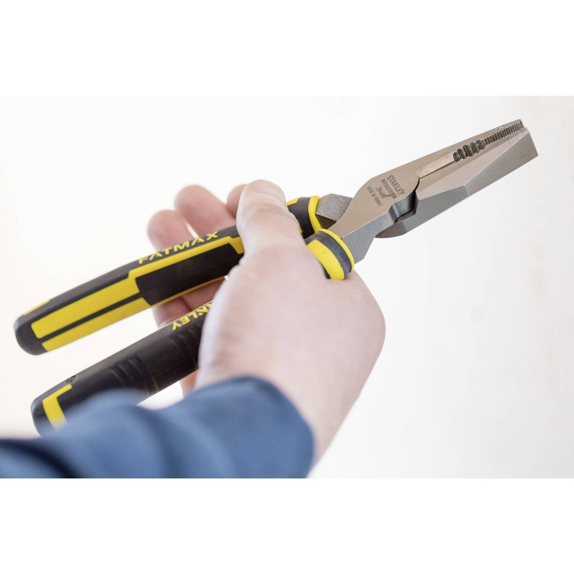 A person is holding a combination pliers with a yellow and black handle, ready to grip or cut materials.