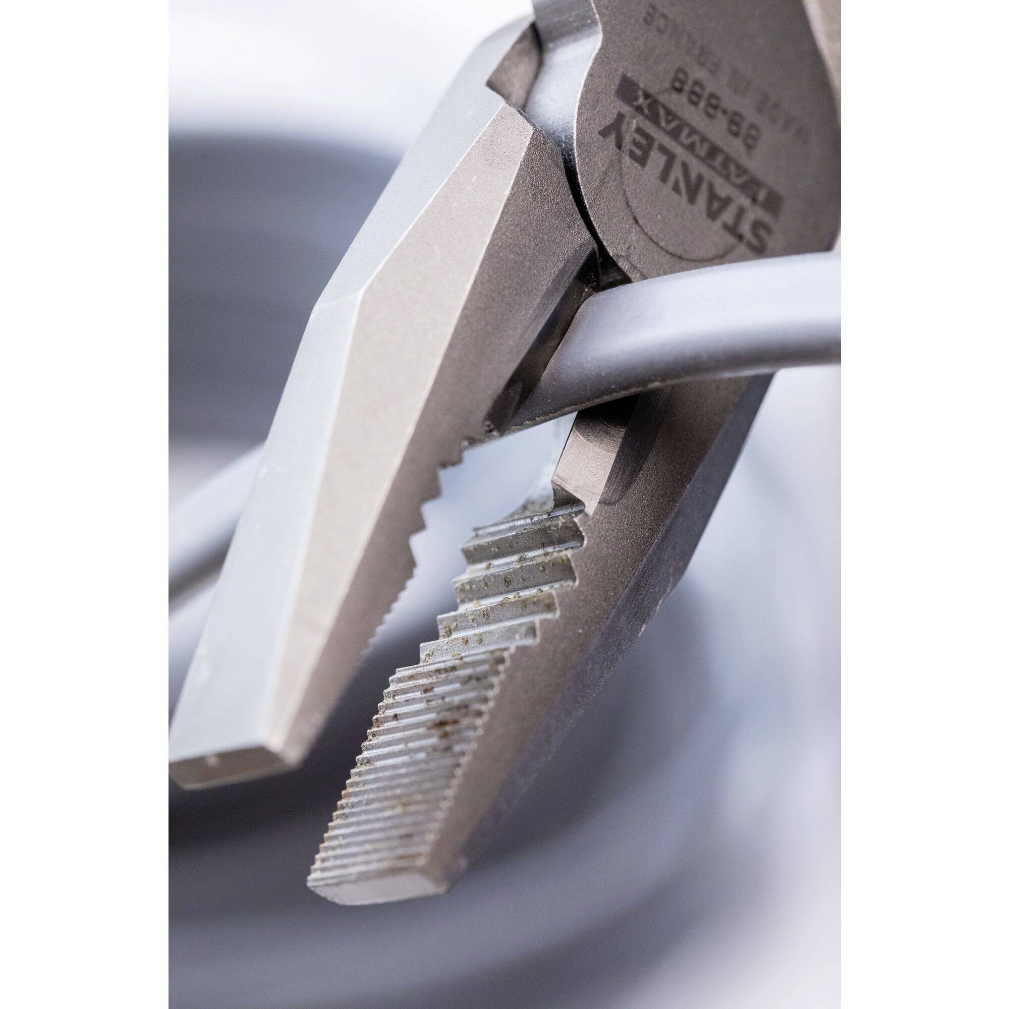 A pair of pliers firmly grips a metal cable, focusing on the serrated jaws and the cable held in the grip.