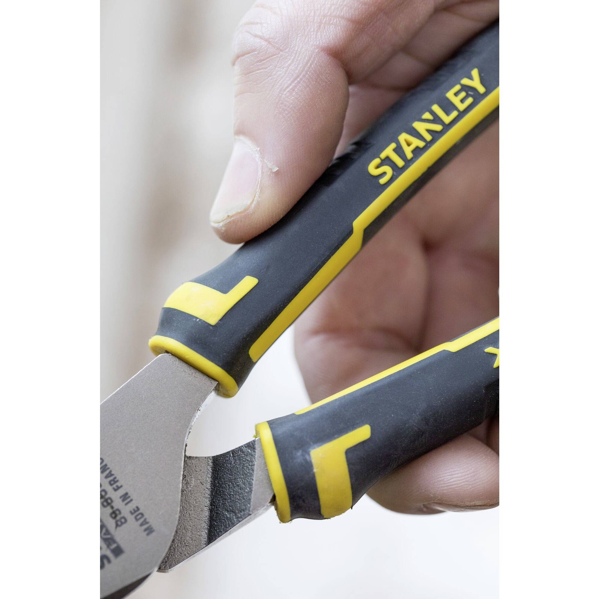 Close-up of a hand firmly gripping a 'Stanley' pliers, focused on the yellow and black handles.