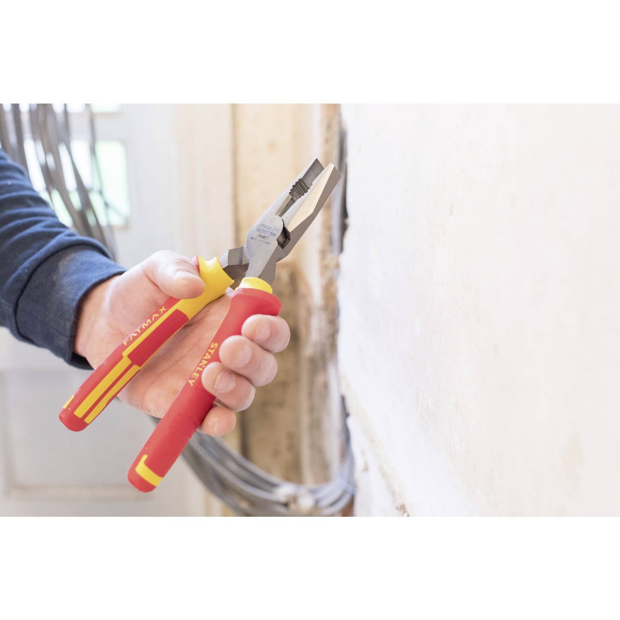 A person is holding a red adjustable spanner and cutting a cable inside a room. Walls and cables are visible in the background.