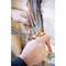 Two hands are using pliers to bend copper wires. The background shows exposed wall structures with multiple cables.