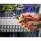 A hand holds a side cutter and cuts a cable in front of a control panel with colourful cables.