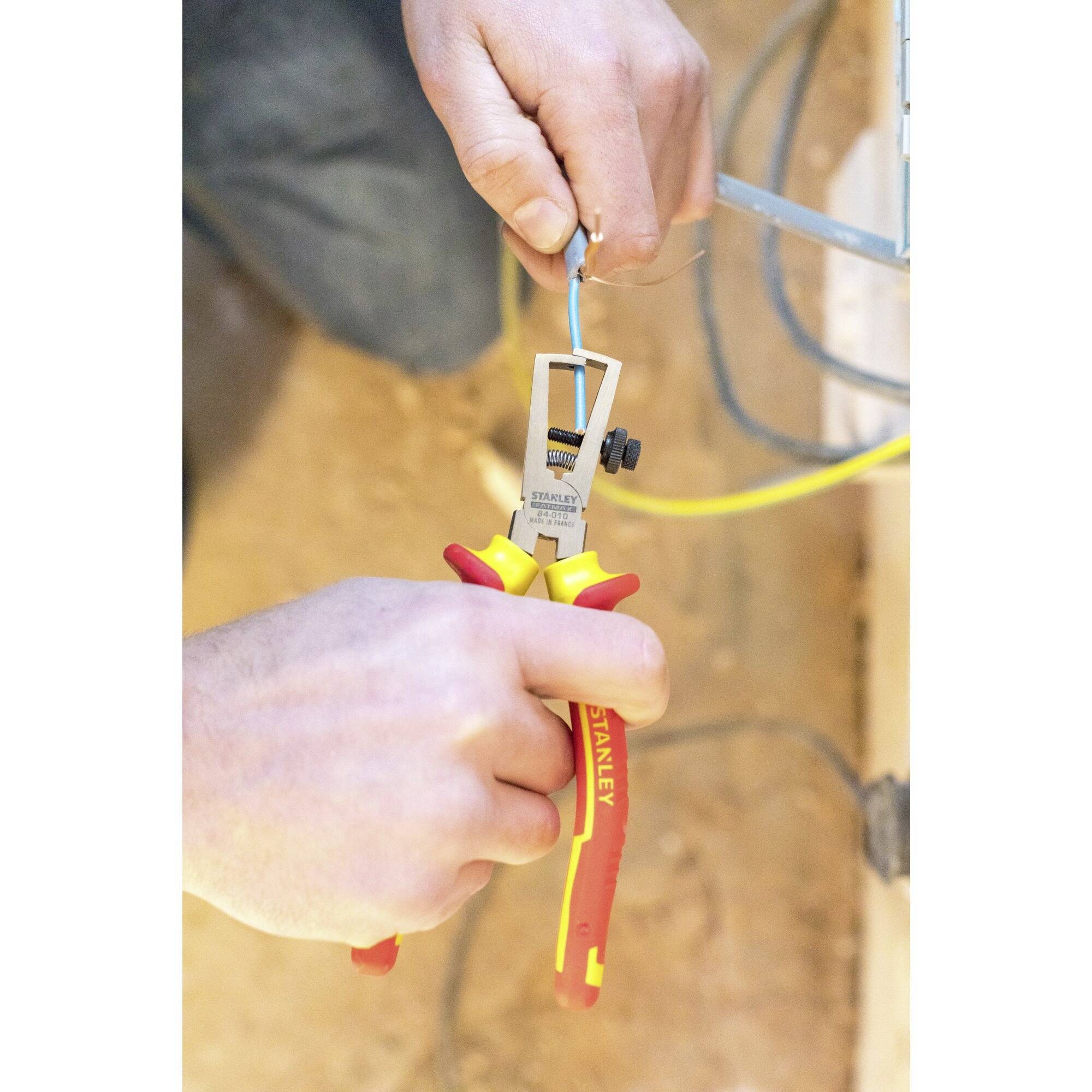 A tradesman is using a multi-tool to work on a cable in an exposed wall. The tool has red and yellow handles.