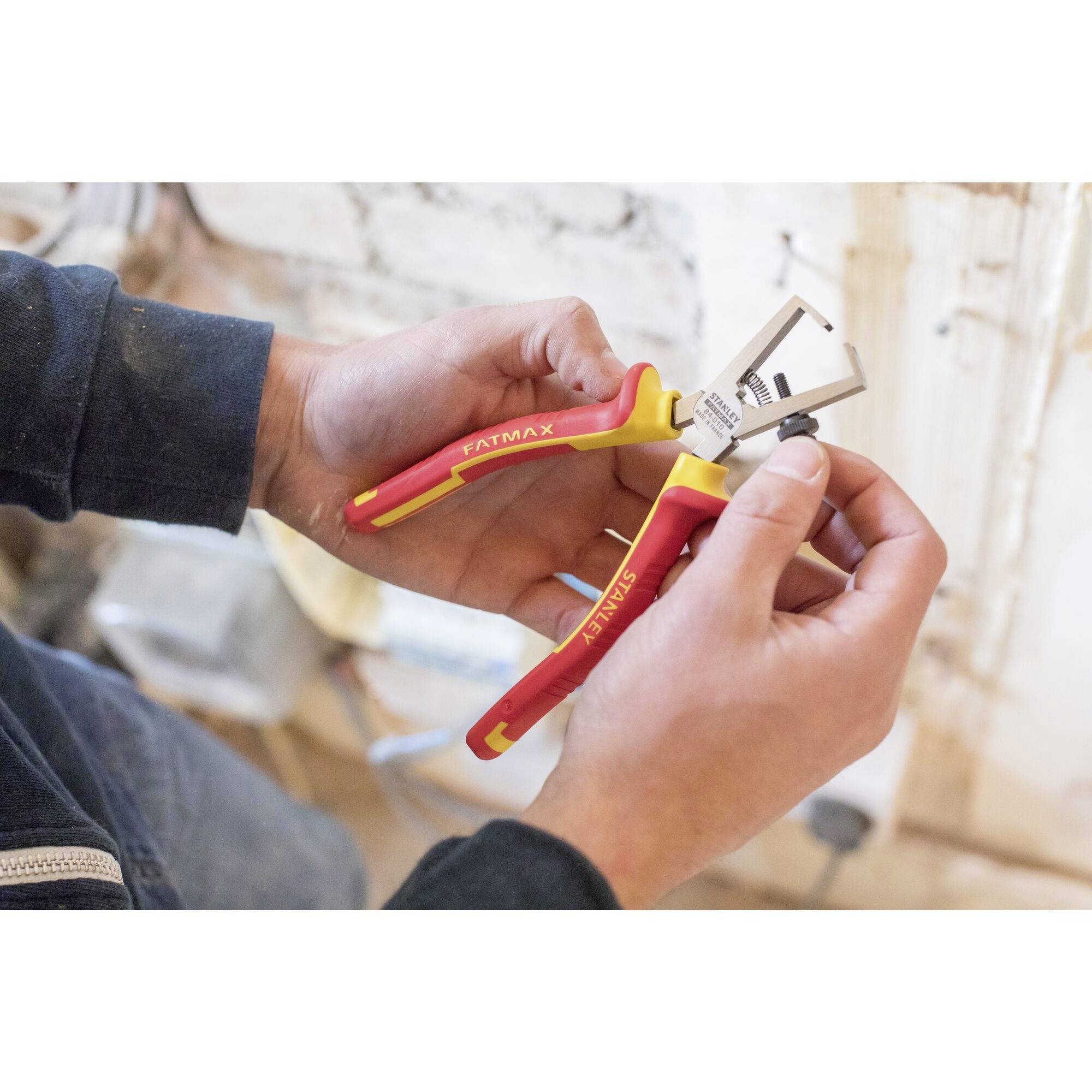 A person is holding a red and yellow side cutters with the 'FATMAX' label. They are in a workshop or construction site.