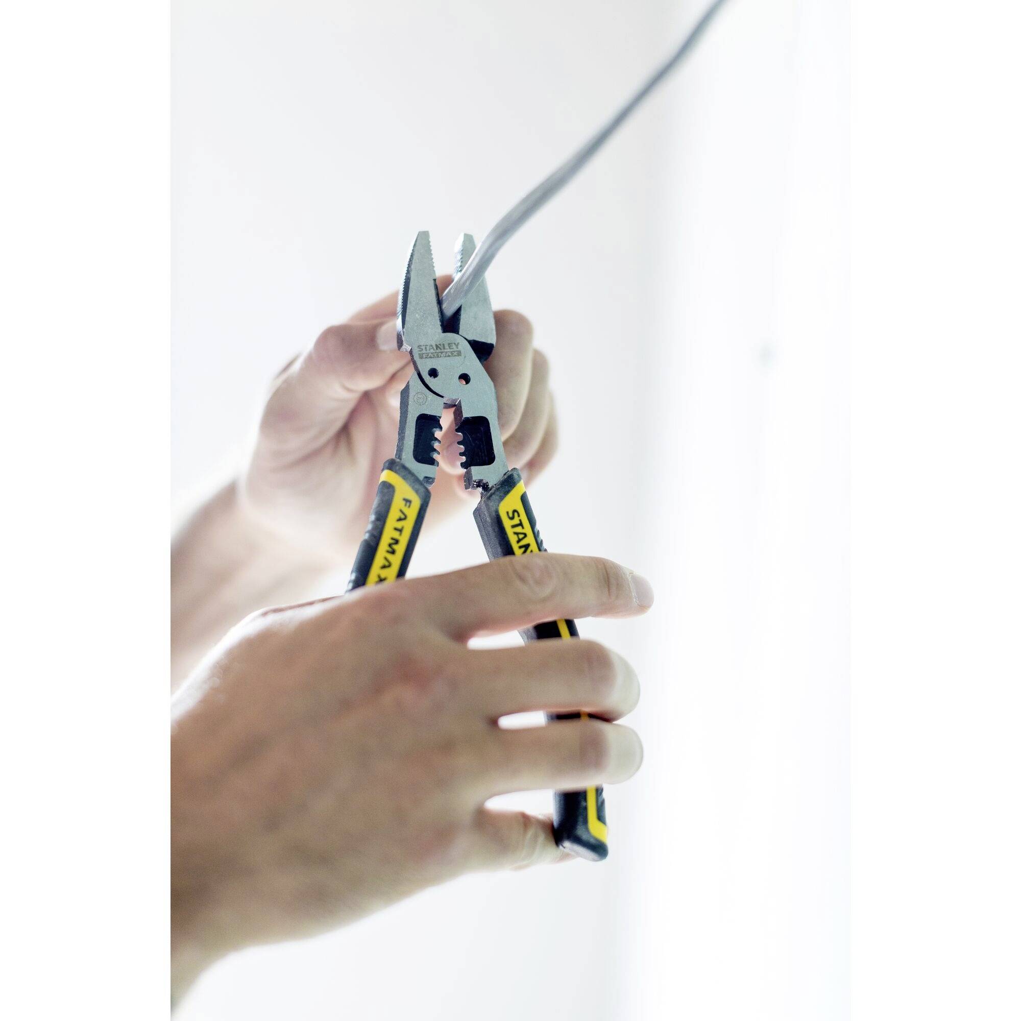 A person is using wire strippers to work on a cable. The tool has a yellow handle and a metal head.
