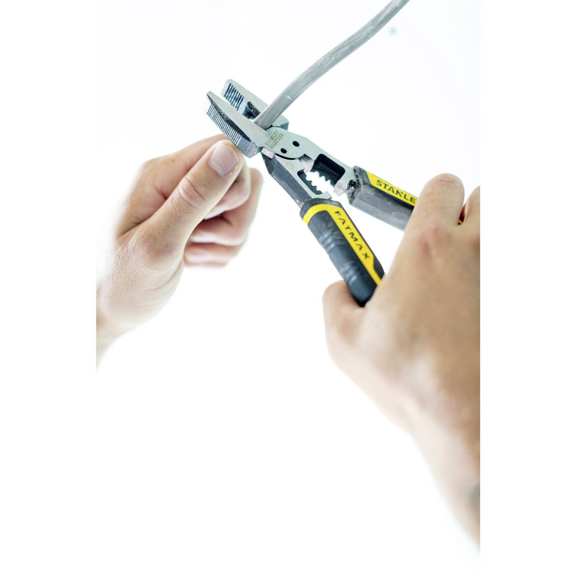 Two hands are holding a pair of pliers and cutting a cable. The pliers have yellow handles, and the cable is grey.