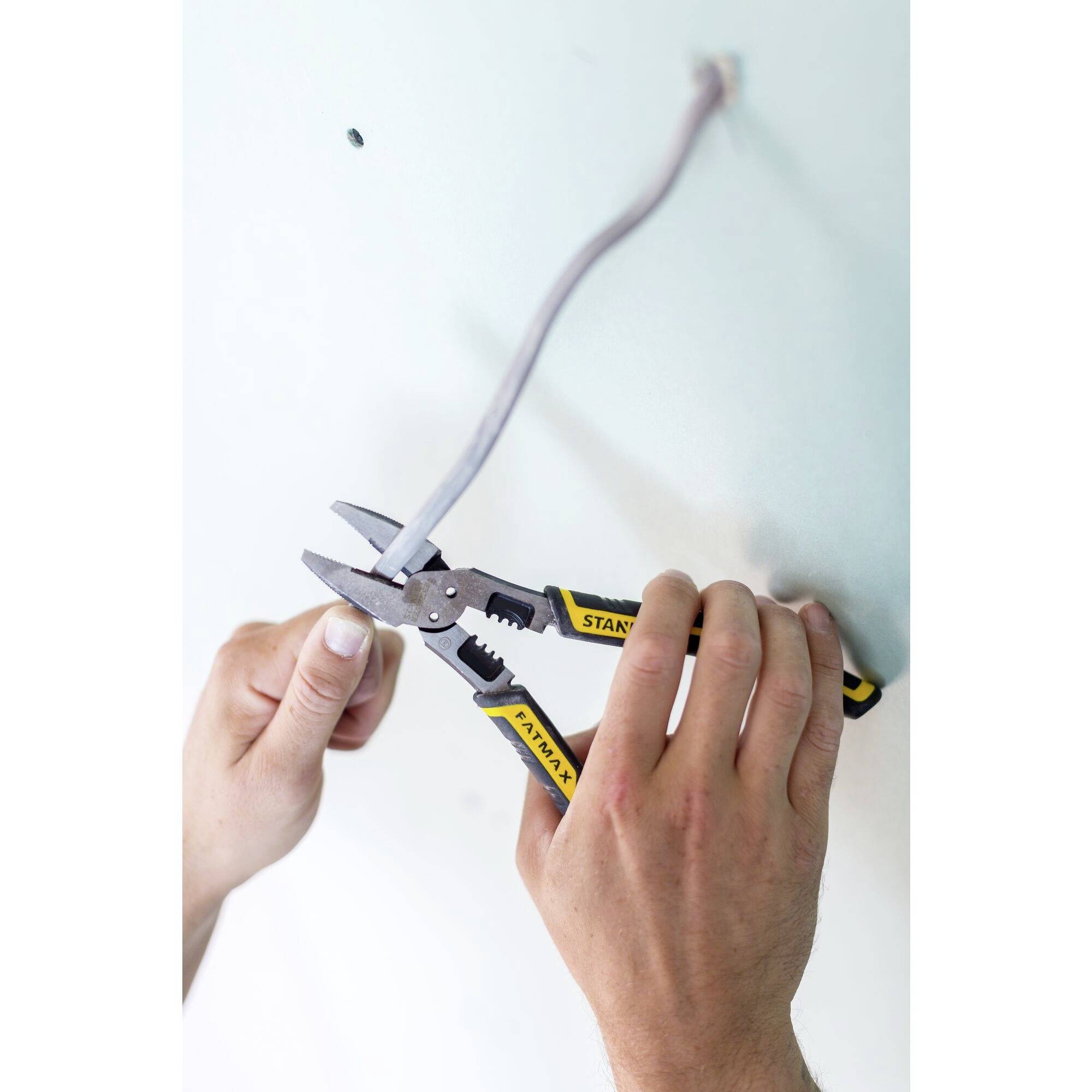 A person is holding pliers and cutting a grey cable on a wall.