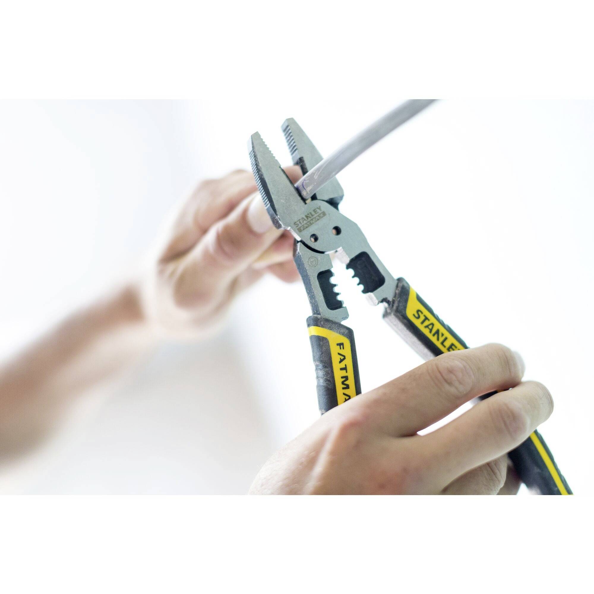 A person is using pliers to cut a grey cable. The pliers have a yellow and black handle.