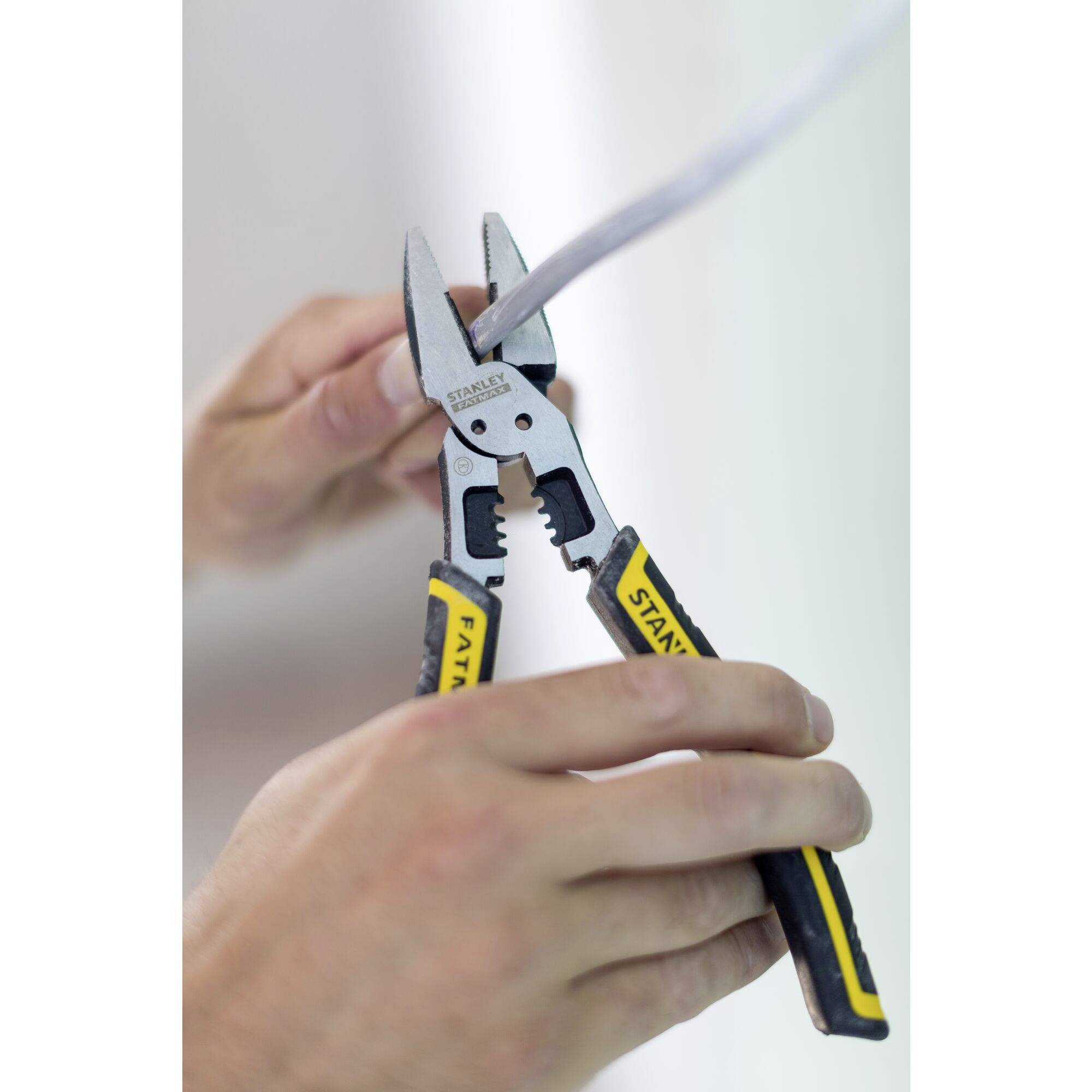 Two hands are holding a pair of pliers cutting a cable. The pliers have black and yellow handles.