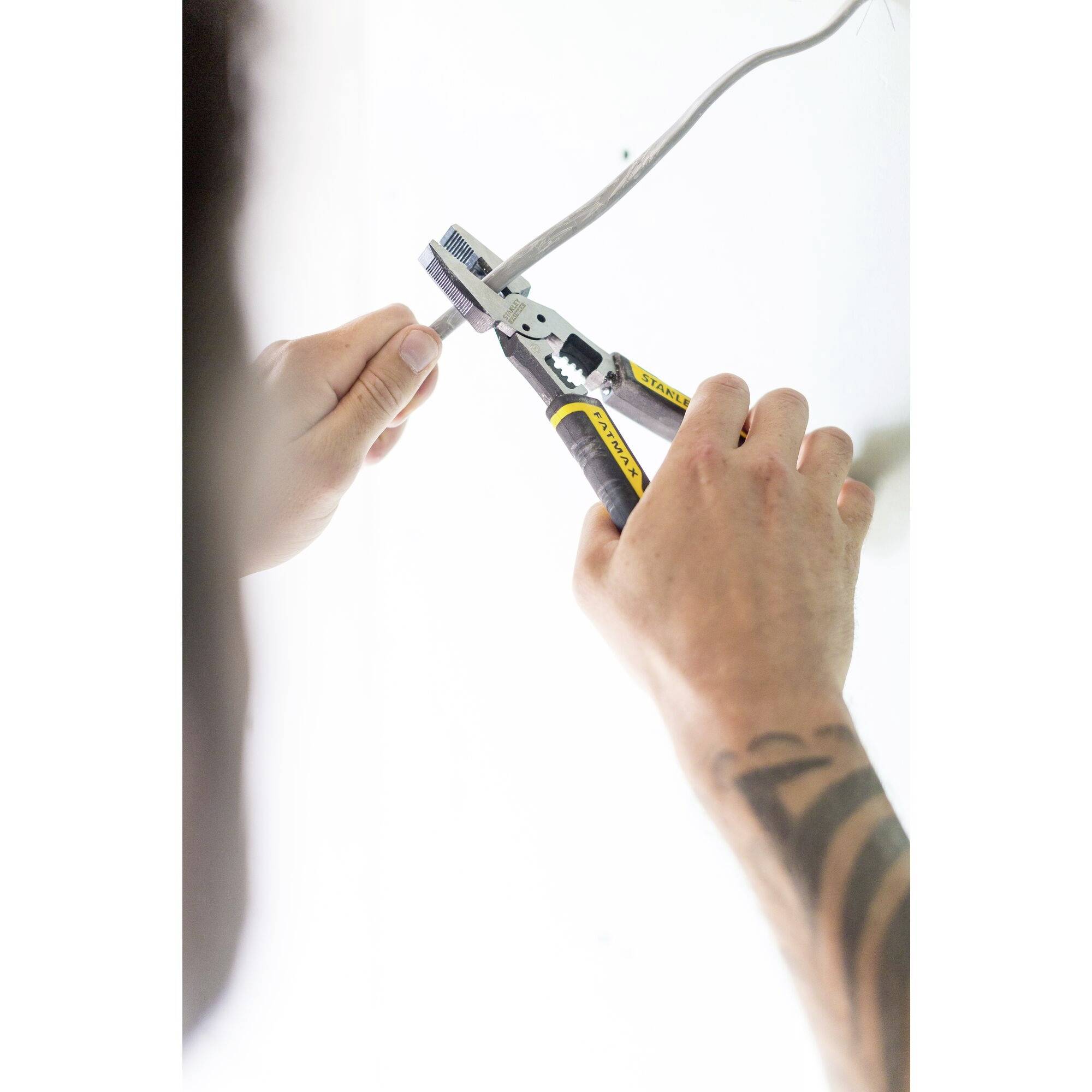 A person is cutting a cable with a yellow side cutters. The focus is on the hands working on the wire.