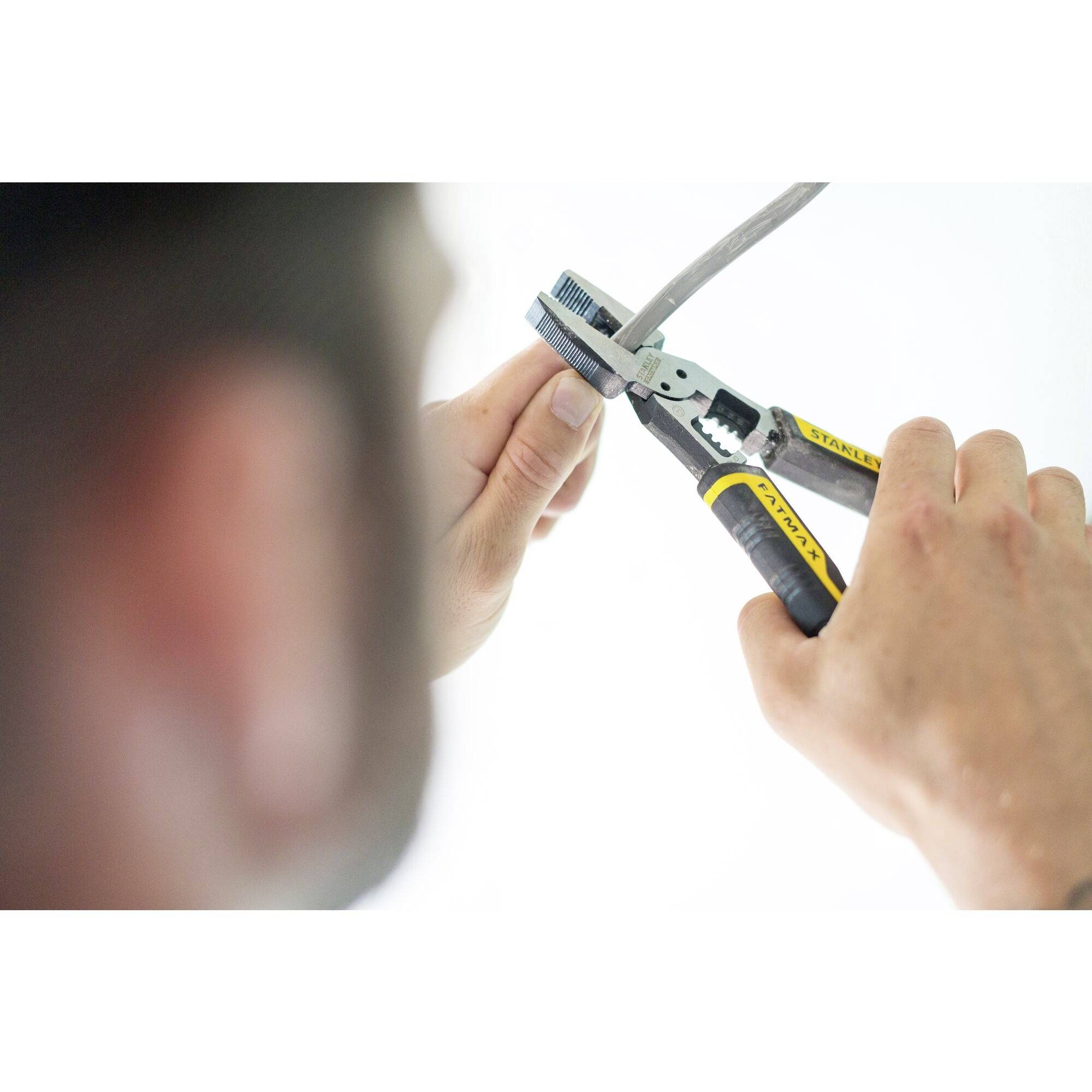 A person is cutting a grey cable with a yellow and black side cutter. The background is out of focus.