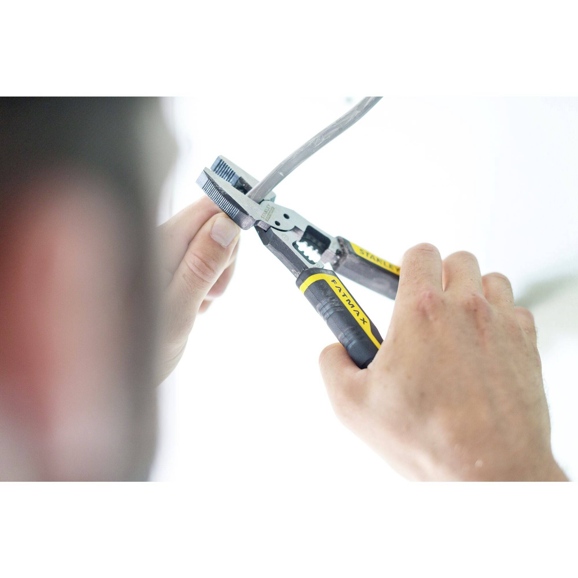 A person is using pliers to cut or work on a cable. The cable is being held carefully and the pliers are positioned.