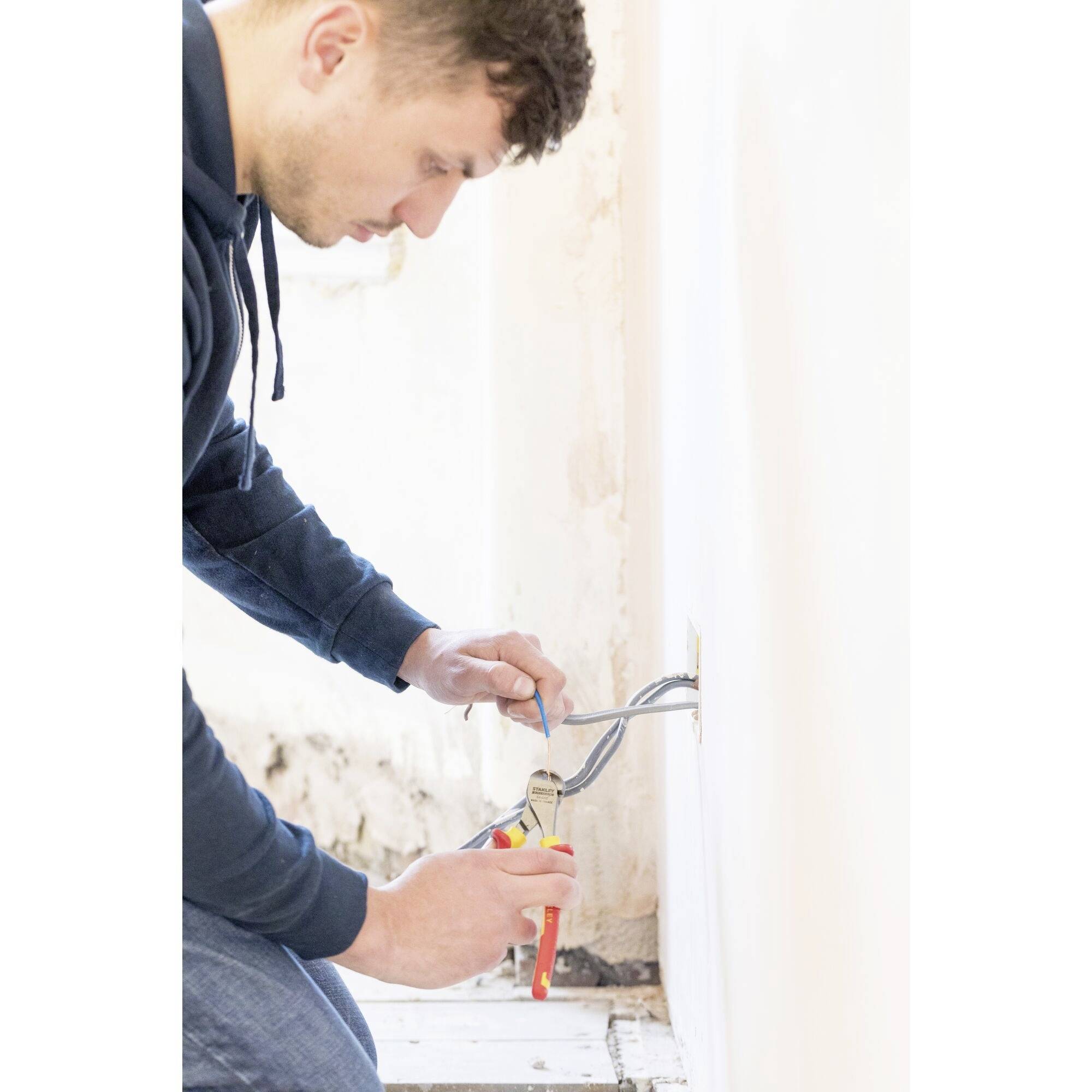 A person wearing a blue hoodie is working with a screwdriver on a socket and cables in a renovated room.