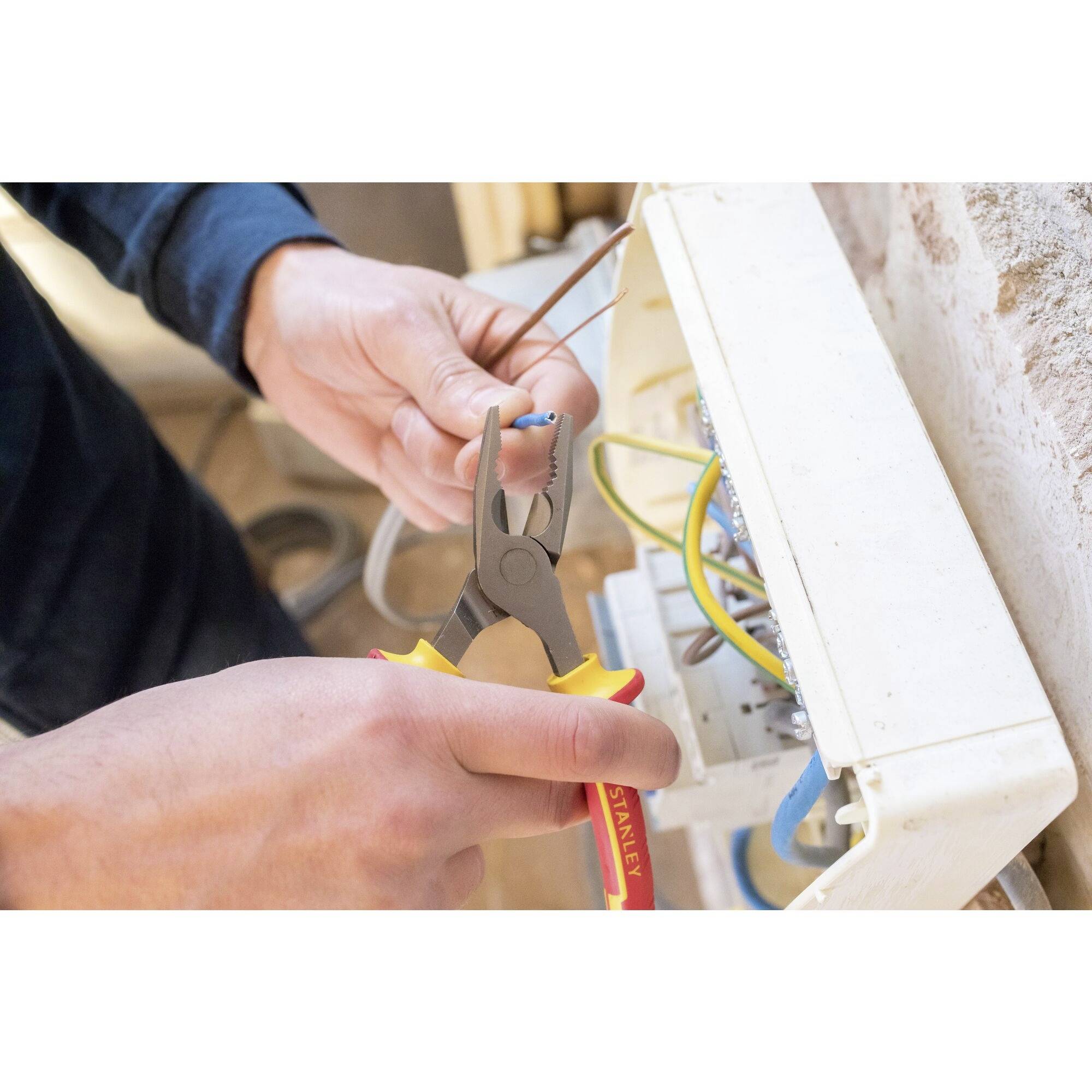 An electrician is working on an open fuse box. He is holding a wire with pliers and connecting electrical connections.