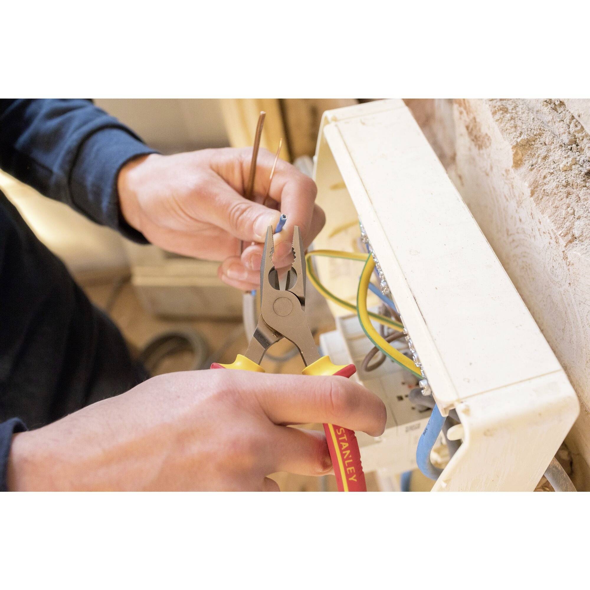 A person is repairing electrical wiring with pliers. Hands are holding cables and tools next to an open cover.