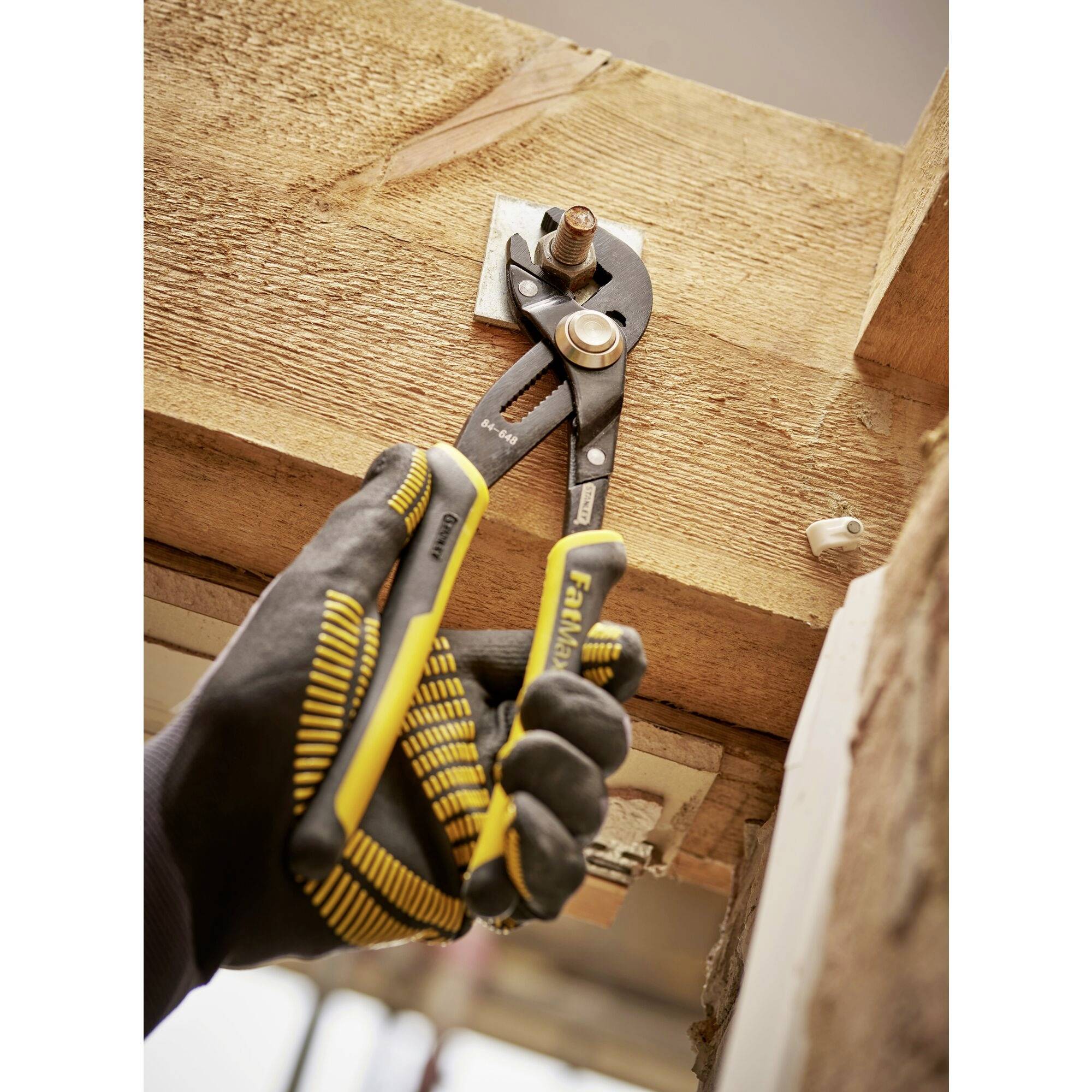 A spanner is used to tighten a nut on a wooden beam. The person is wearing protective gloves.
