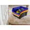 Several colourful storage boxes are stacked on a wooden floor, with the front box containing a tape measure and extension lead.