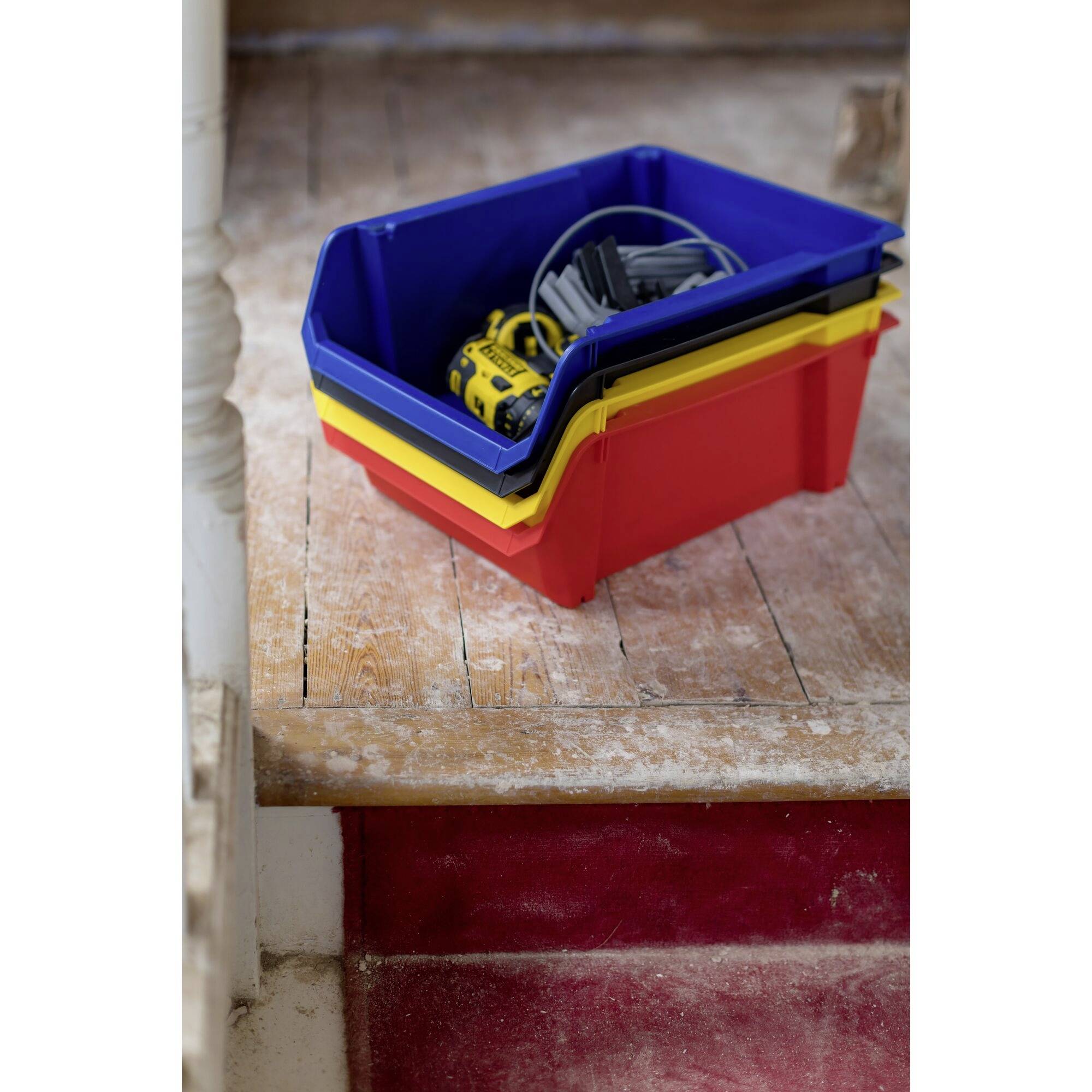 Stacked colourful plastic storage boxes on a wooden staircase, filled with tools and cables. Environment in a state of renovation.