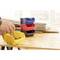 Small stacked containers in blue, red, black and yellow are standing on a wooden table. A hand is placing screws into the yellow container.