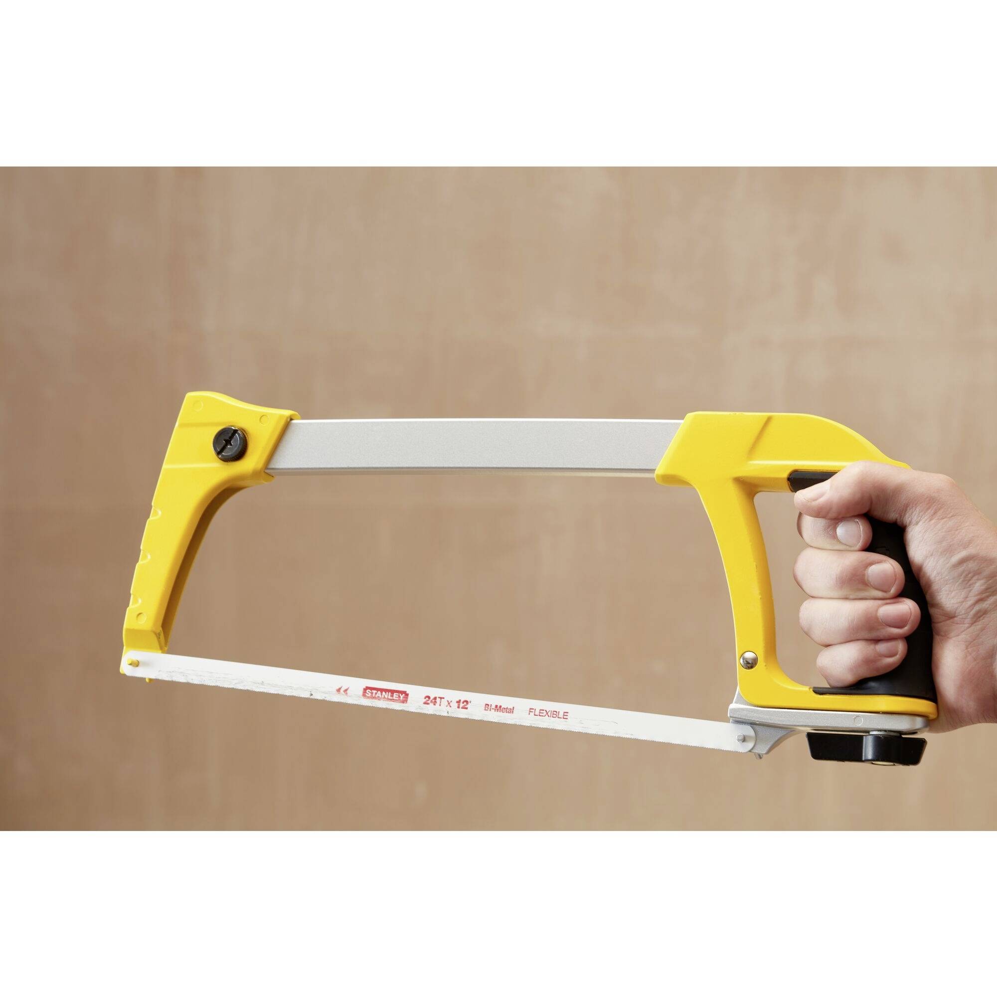 A person is holding a yellow metal saw with a steel frame and a red saw blade, ready for use.