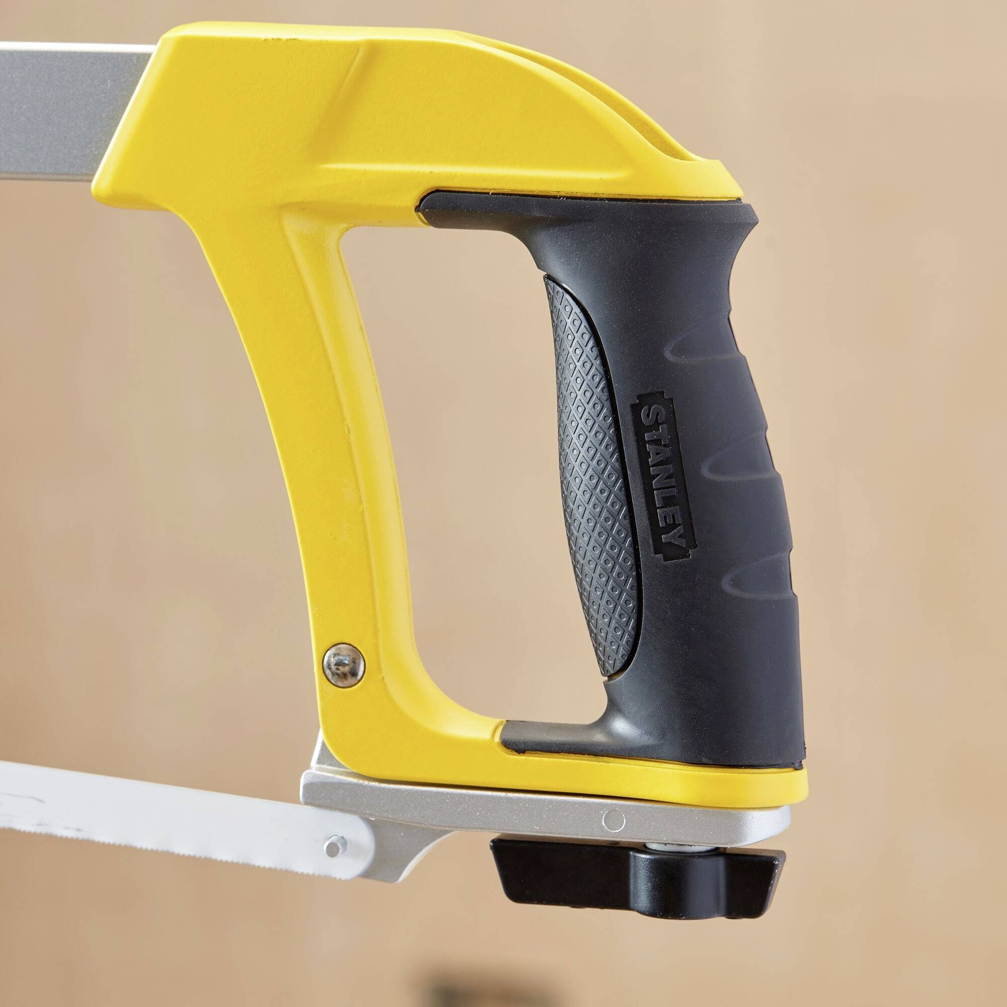 A yellow handsaw with a black handle and silver blade, suitable for woodworking. Blurred wooden background in the backdrop.