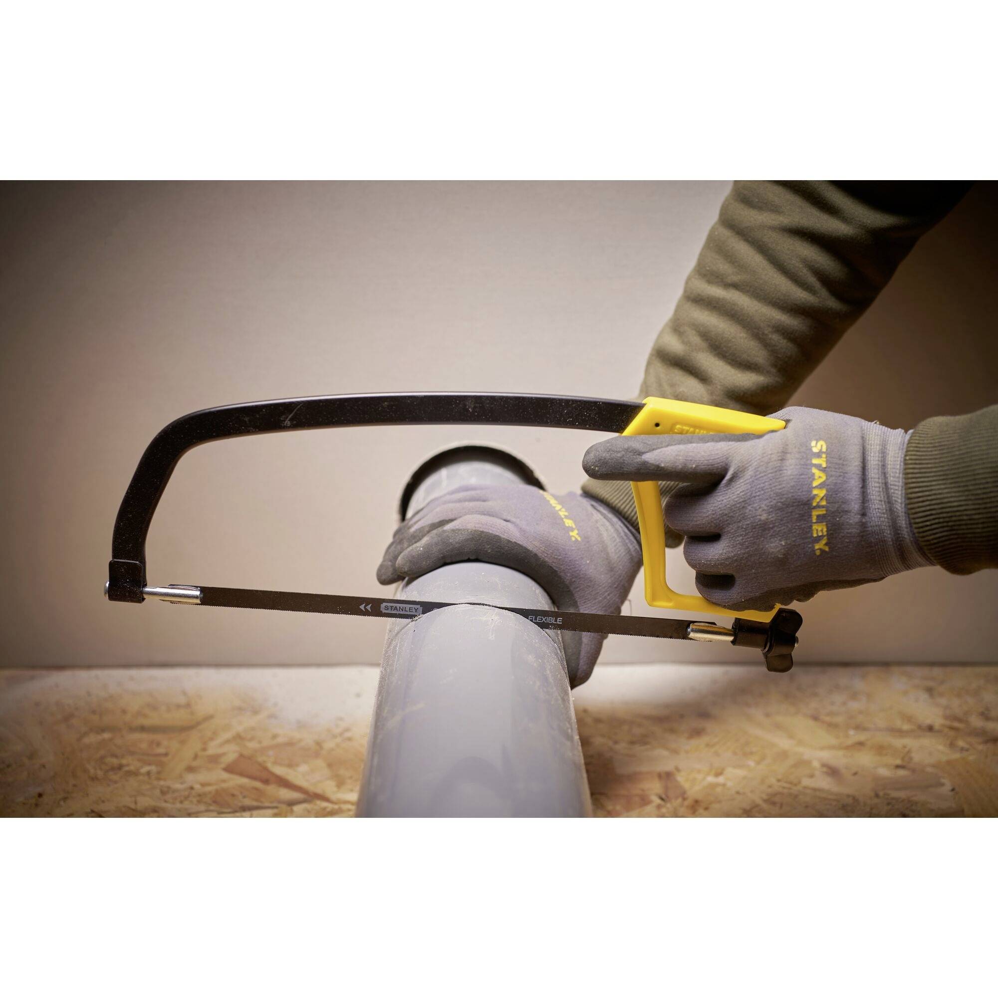 A person is cutting a grey pipe with a metal saw. The hands are wearing grey gloves.